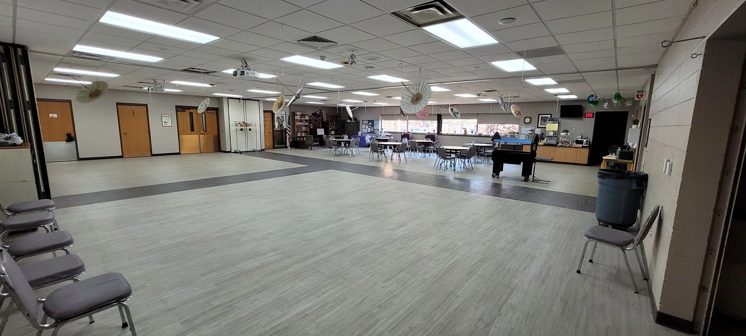 A large space with some tables and chairs set up, large open areas, and windows along one side