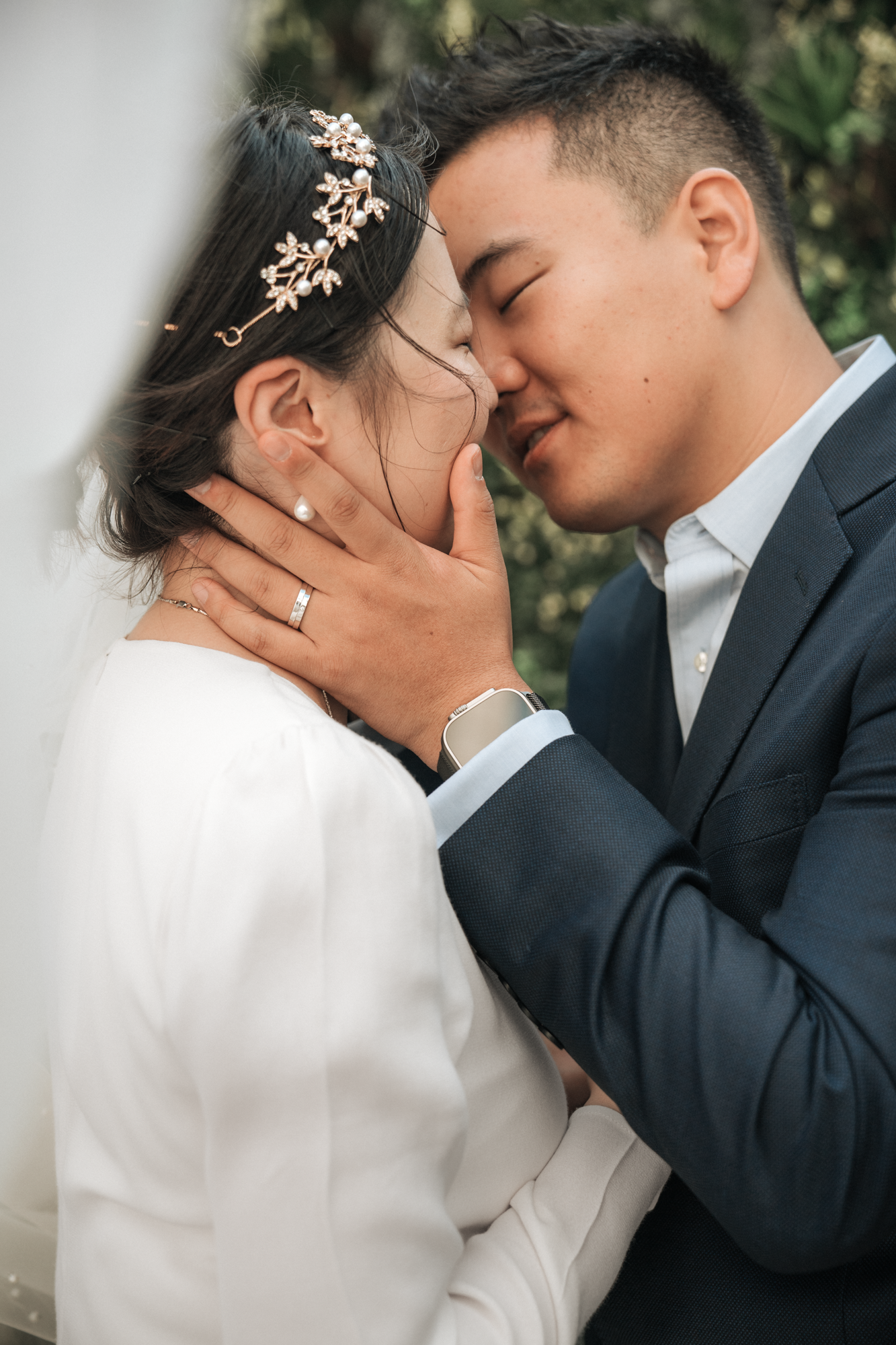 A couple sharing a romantic moment outdoors, touching foreheads and holding each other's faces gently.