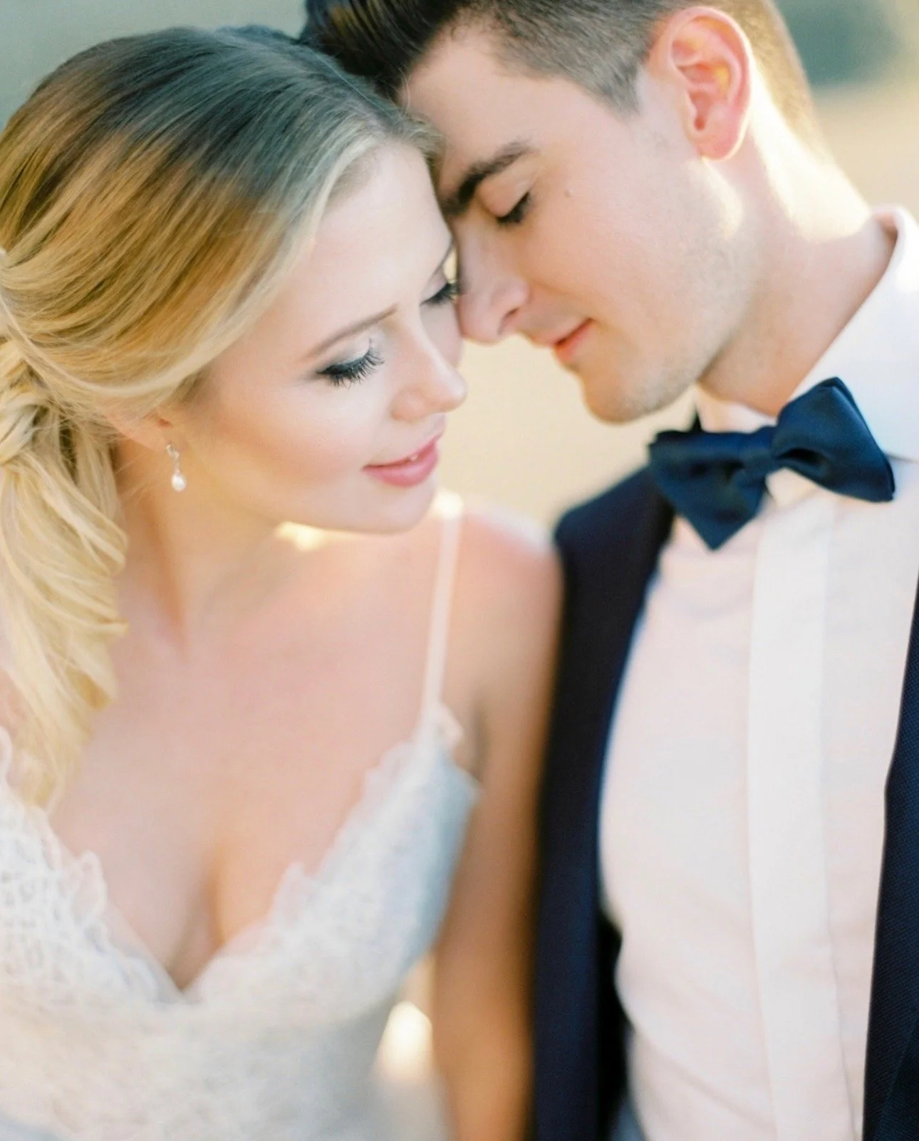 A close-up of a bride and groom with foreheads touching, eyes closed, embracing on their wedding day.