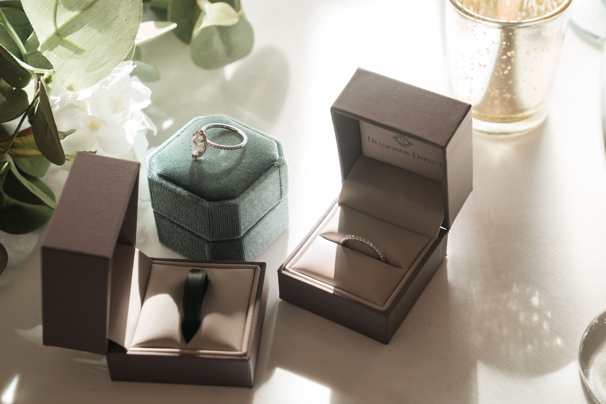 Open jewelry boxes with engagement rings, surrounded by flowers and candles.