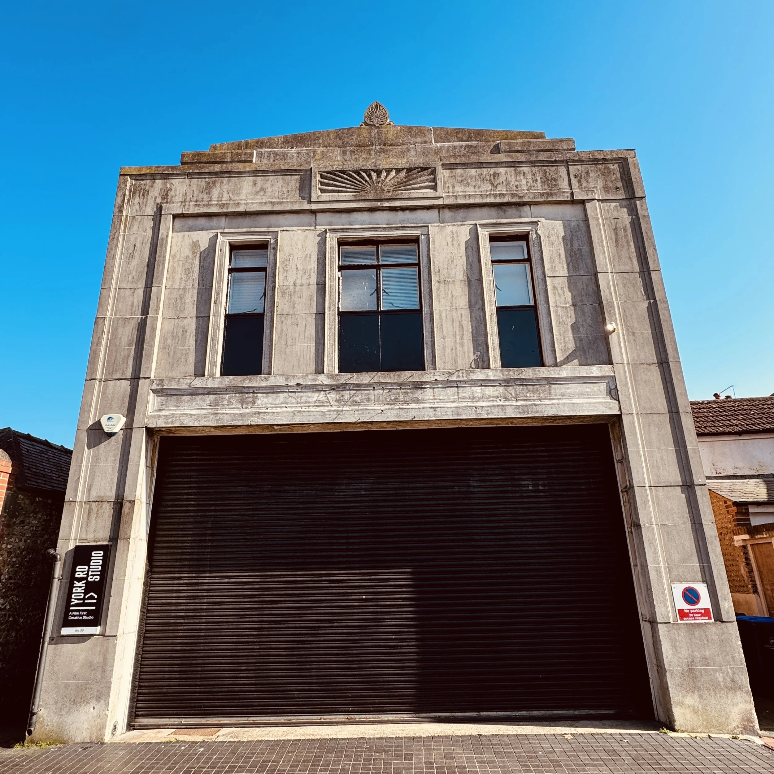 Facade of a building with two windows and a large black roll-up door, under a clear blue sky. Signage indicates it is a creative studio called York Road Studio.