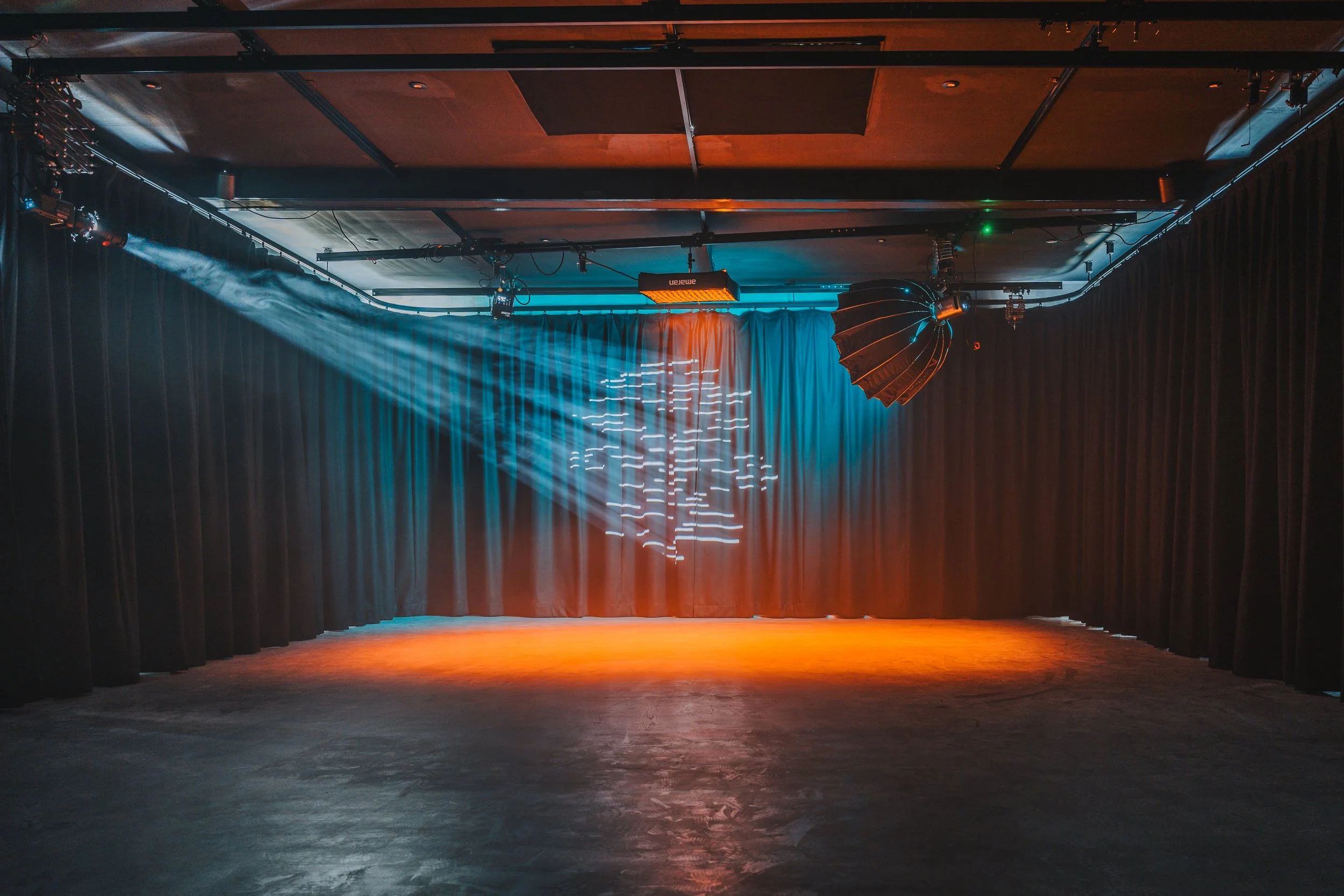 Empty stage with black curtains, stage lights, and a wooden floor, ready for a performance.