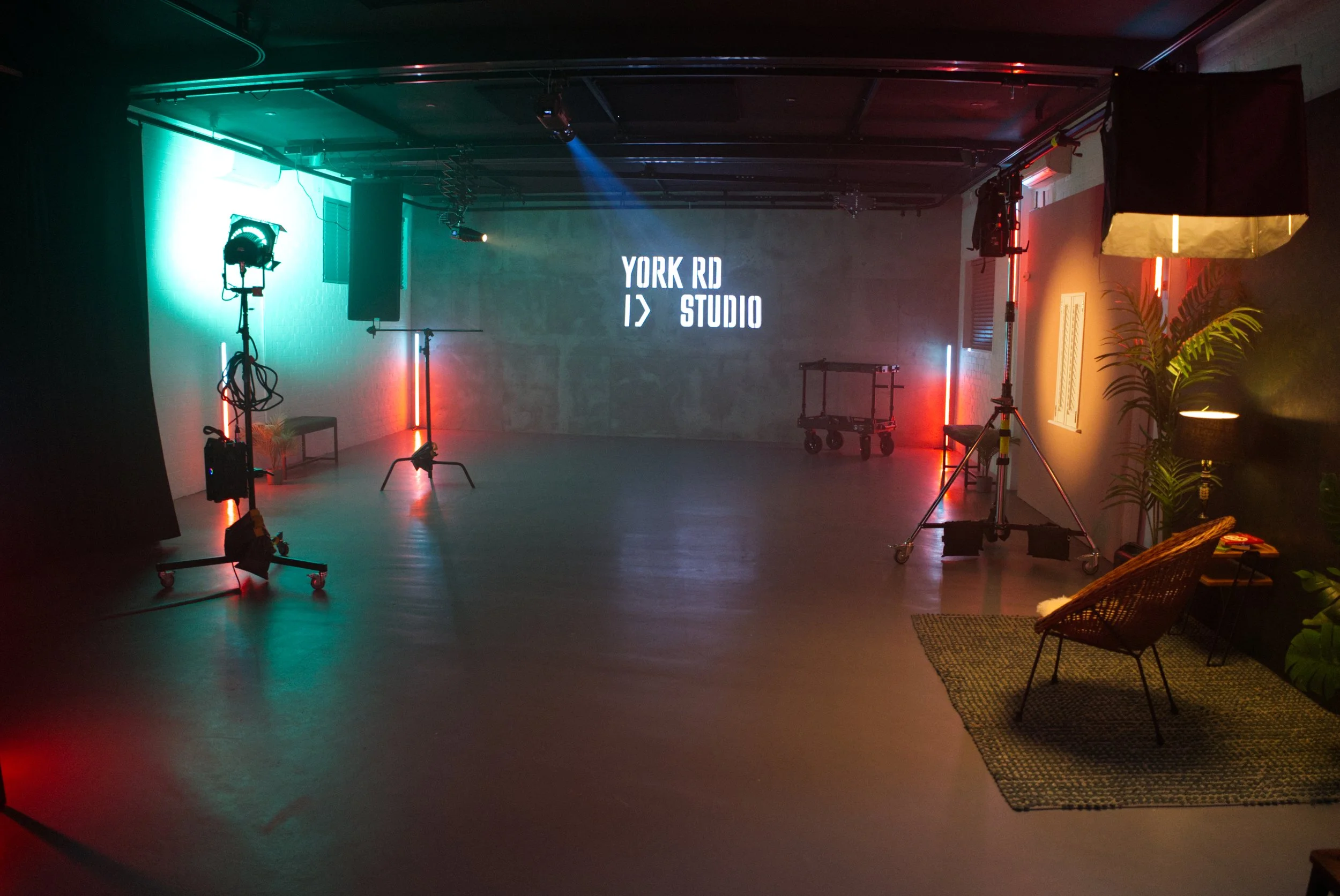 Empty studio space with colored lighting, camera equipment, and a screen displaying 'YORK RD   STUDIO' on a textured wall.