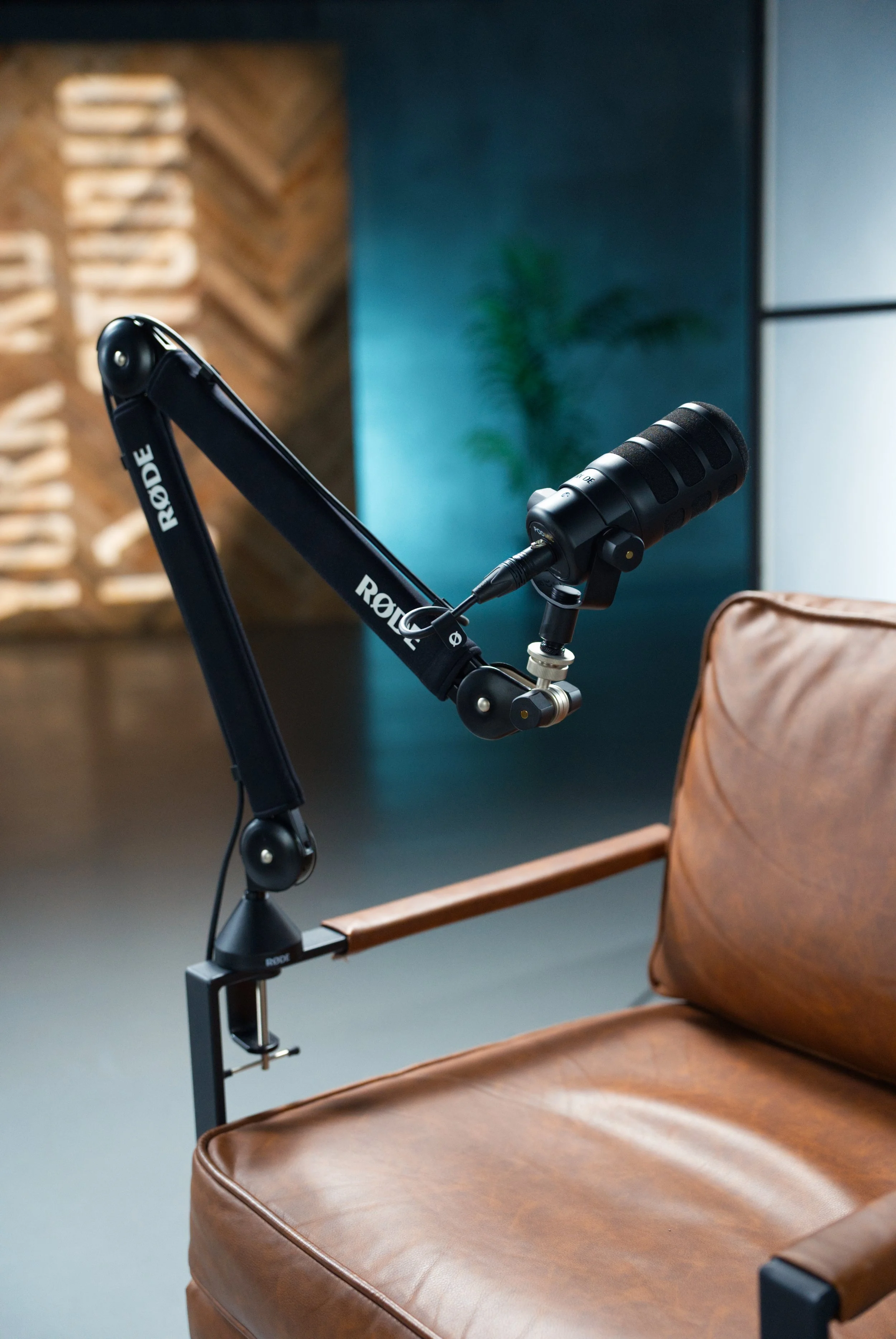 A talk microphone attached to a stand next to a brown leather chair in a professional recording or podcast studio environment.