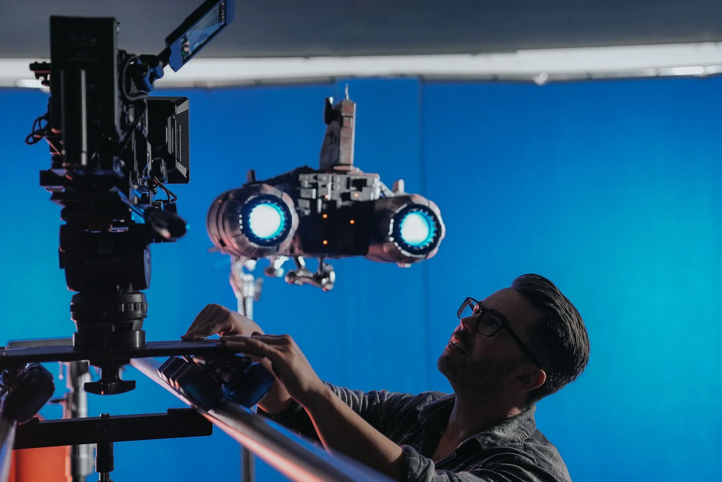 A person working with a camera rig and a robot model suspended in the air, set against a blue background.