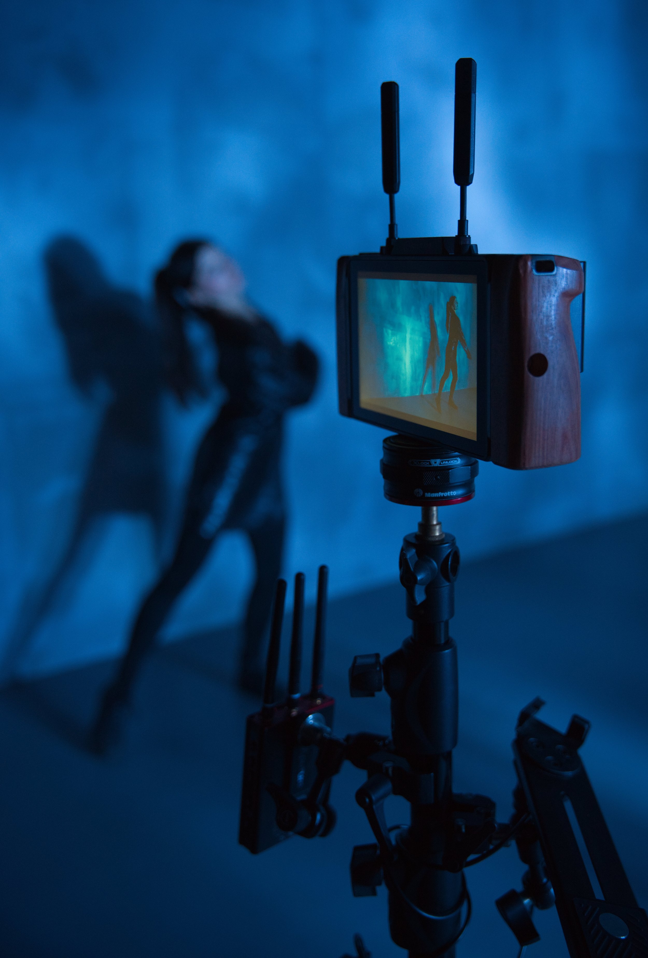 A camera mounted on a tripod capturing a silhouette of a person projected on a screen, against a blue background.