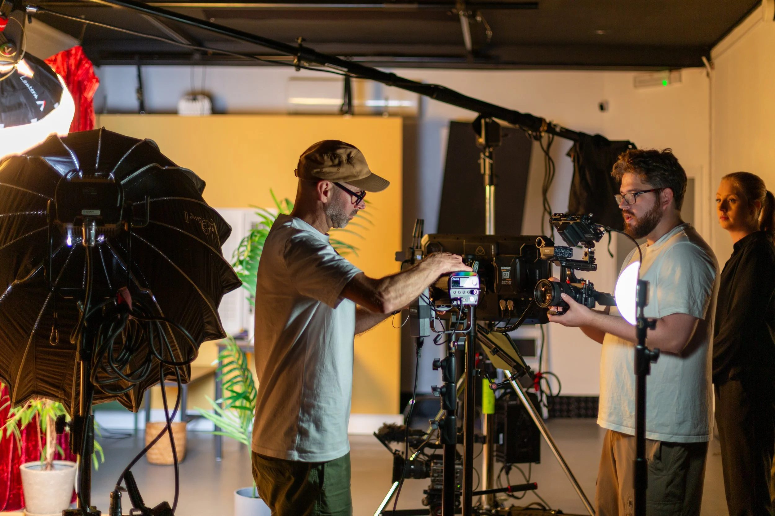 Group of three people working with filmmaking equipment indoors, with plants in the background.