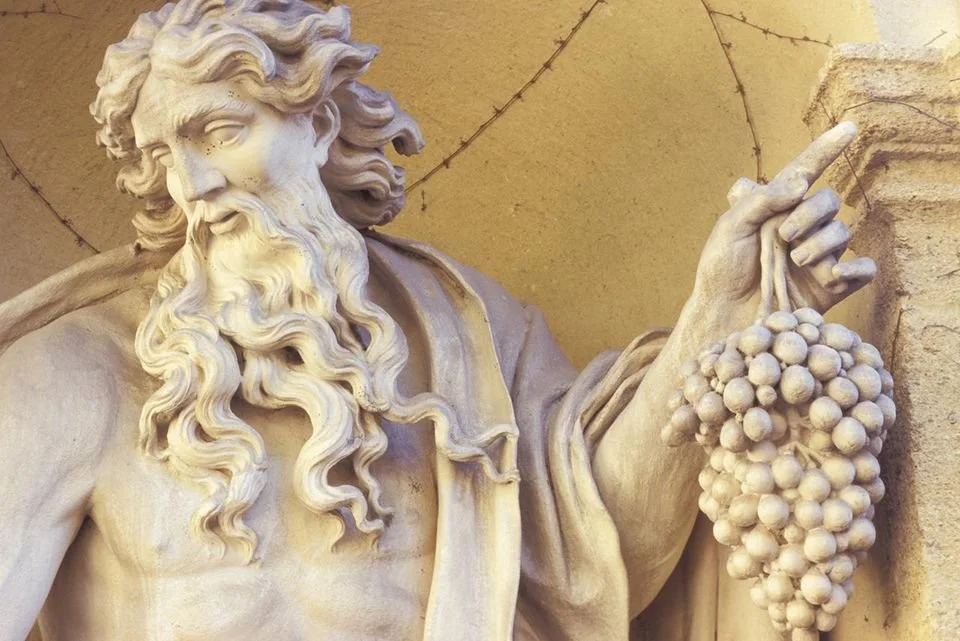 Close-up of a marble sculpture of a bearded man holding a bunch of grapes, possibly depicting the figure of Jesus or a biblical scene, with intricate details and flowing hair.