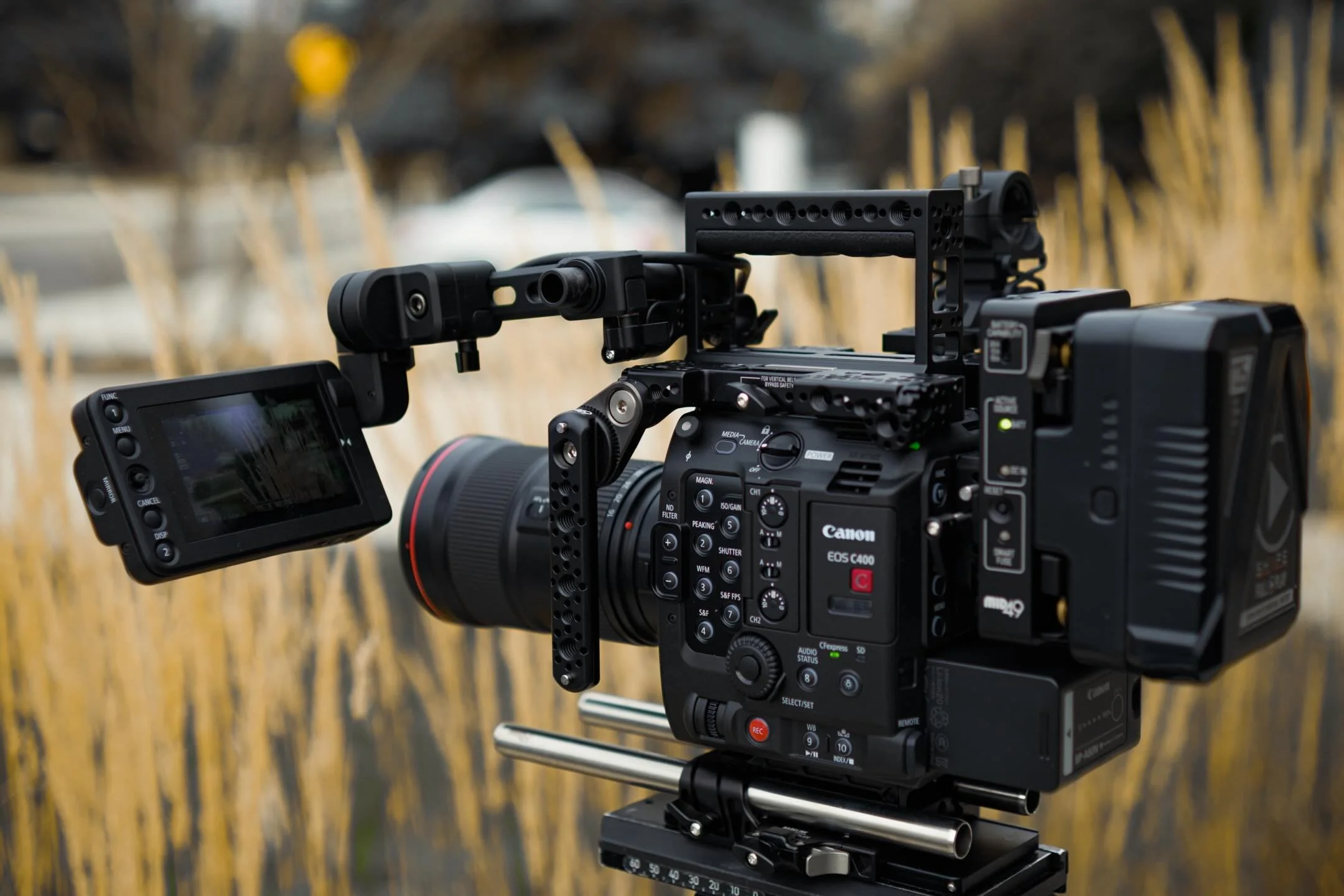 People filming a video outdoors with professional camera equipment and lighting on a grassy field with trees and mountains in the background.