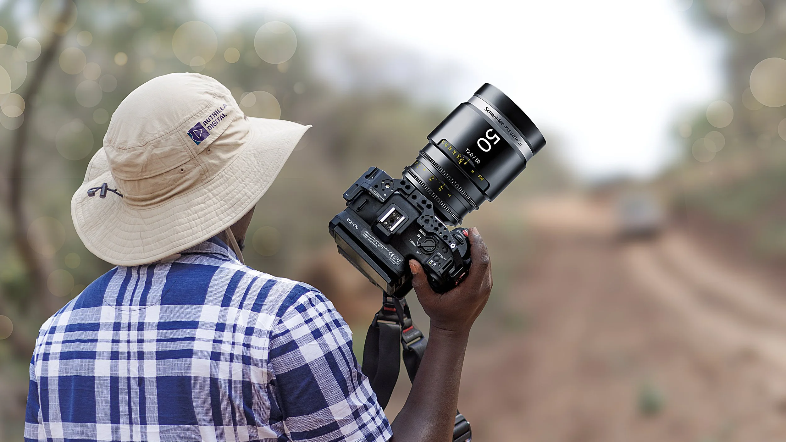 Person wearing a wide-brimmed hat and plaid shirt holding a professional camera outdoors with a blurred natural background.