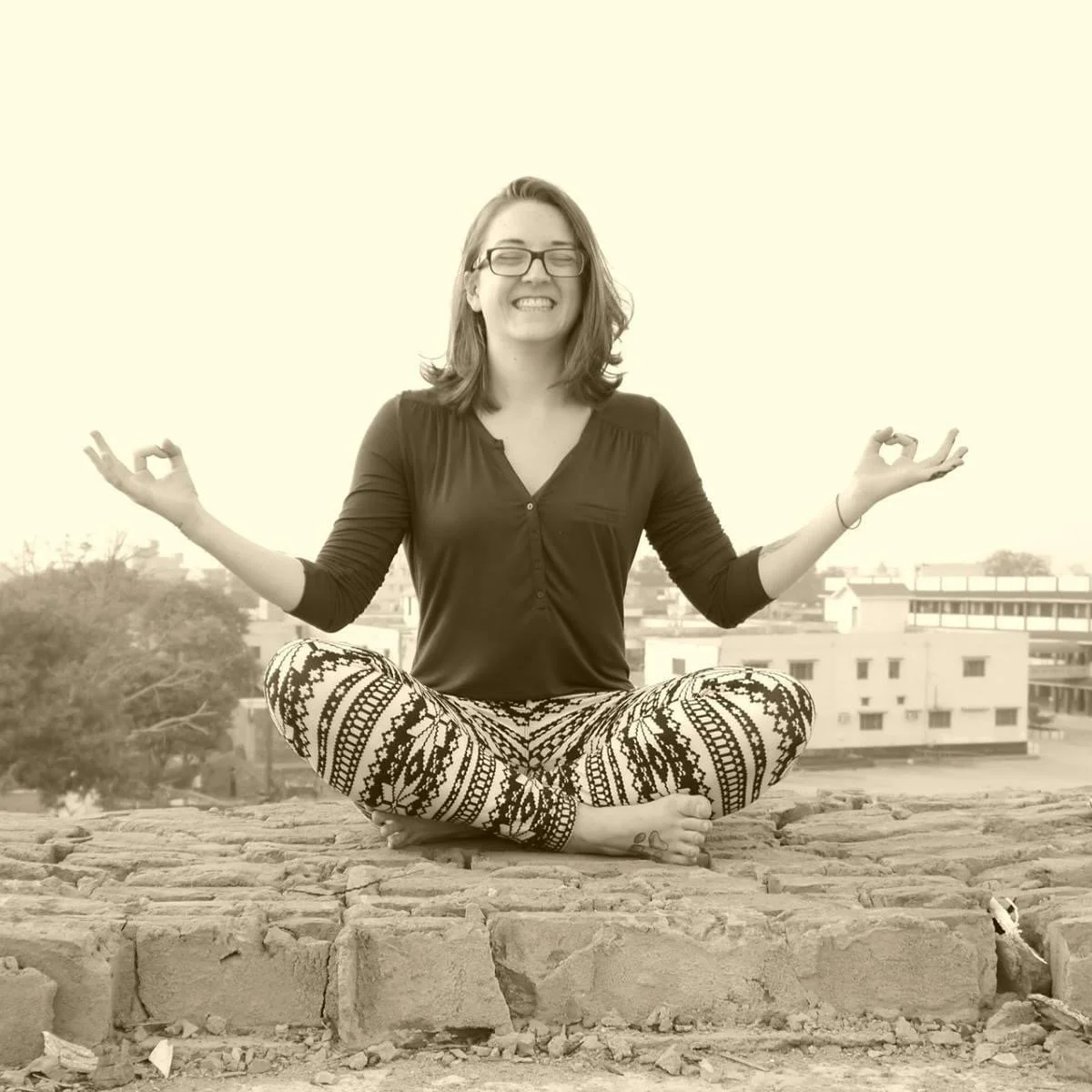 Woman sitting on platform overlooking a city in India, both smiling and using her hands to hold a mudra