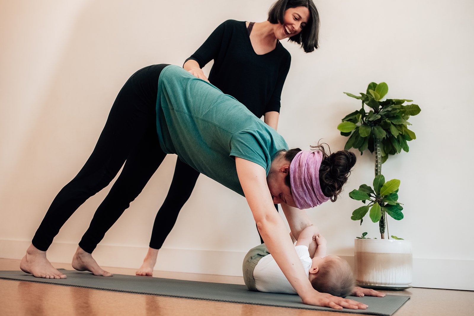 Mother doing Downward facing dog with her baby interacting. Teacher is also interacting with baby