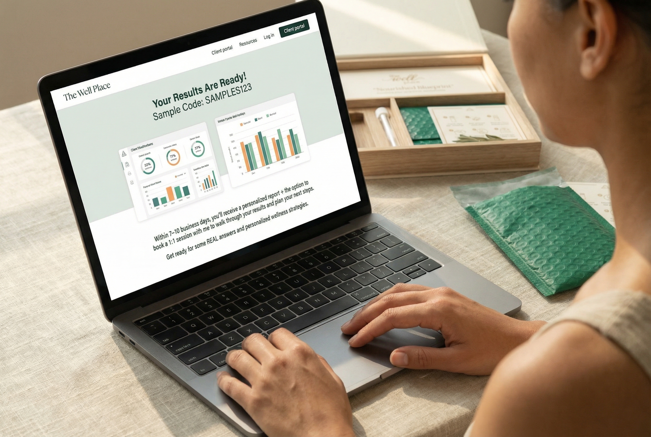 A woman is sitting at a table using a laptop to view a wellness report with bar and pie charts. The screen displays a message indicating that results are ready, with a sample code. There is a wooden tray with a few items and some packaged medical or wellness supplies on the table.