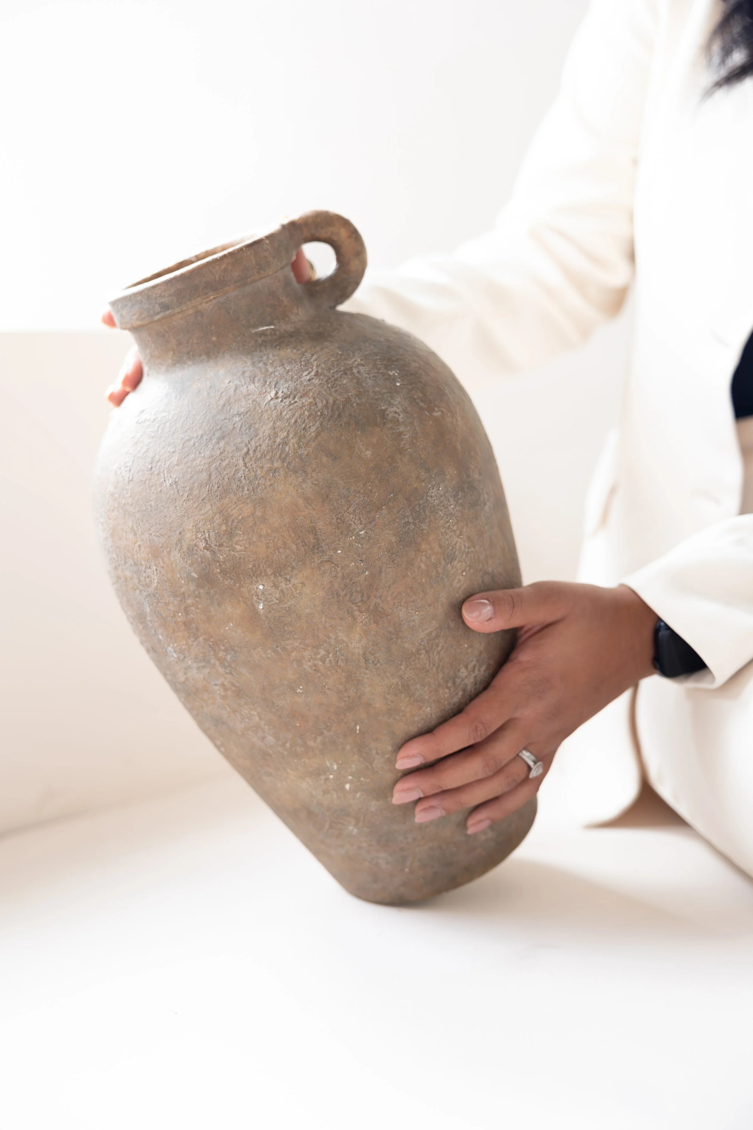 Person holding a large, weathered, brown clay vase with both hands.