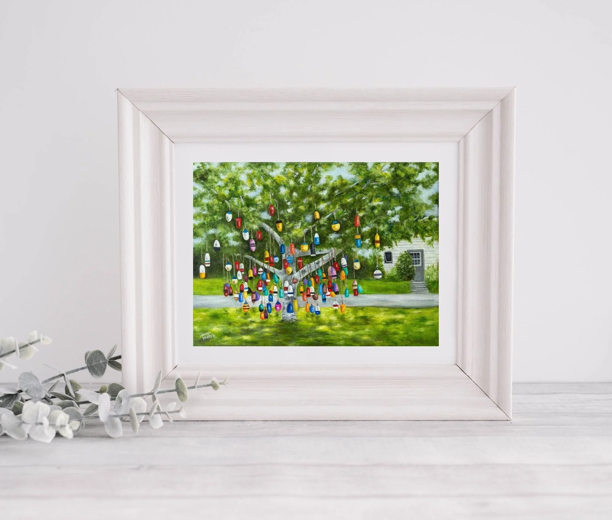 A framed print of a colourful buoy tree in Prince Edward Island, reproduced from an original oil painting featuring colorful hanging fishing buoys beneath a leafy green tree.