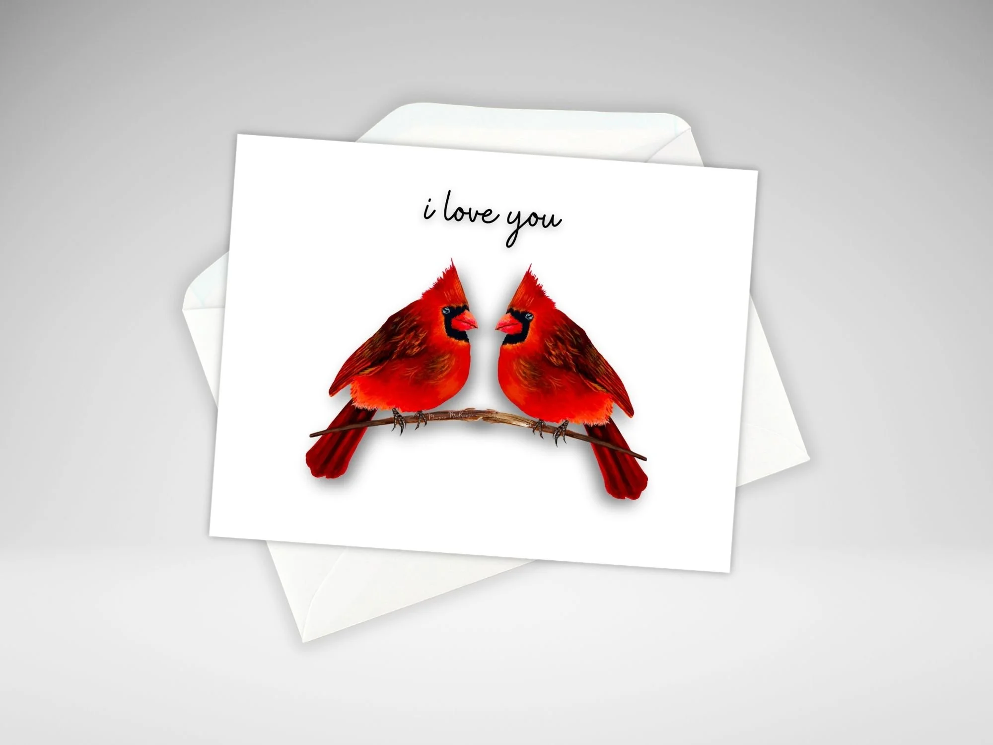 A greeting card by  Maureen Mackenzie featuring two red cardinals perched facing each other on a  branch, set against a  white background. The words I Love You is written just above their heads.