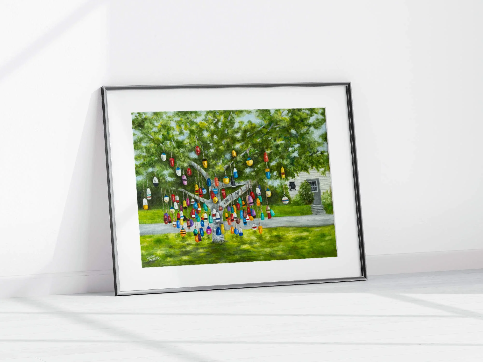 A framed print of a colourful buoy tree in Prince Edward Island, reproduced from an original oil painting featuring colorful hanging fishing buoys beneath a leafy green tree.