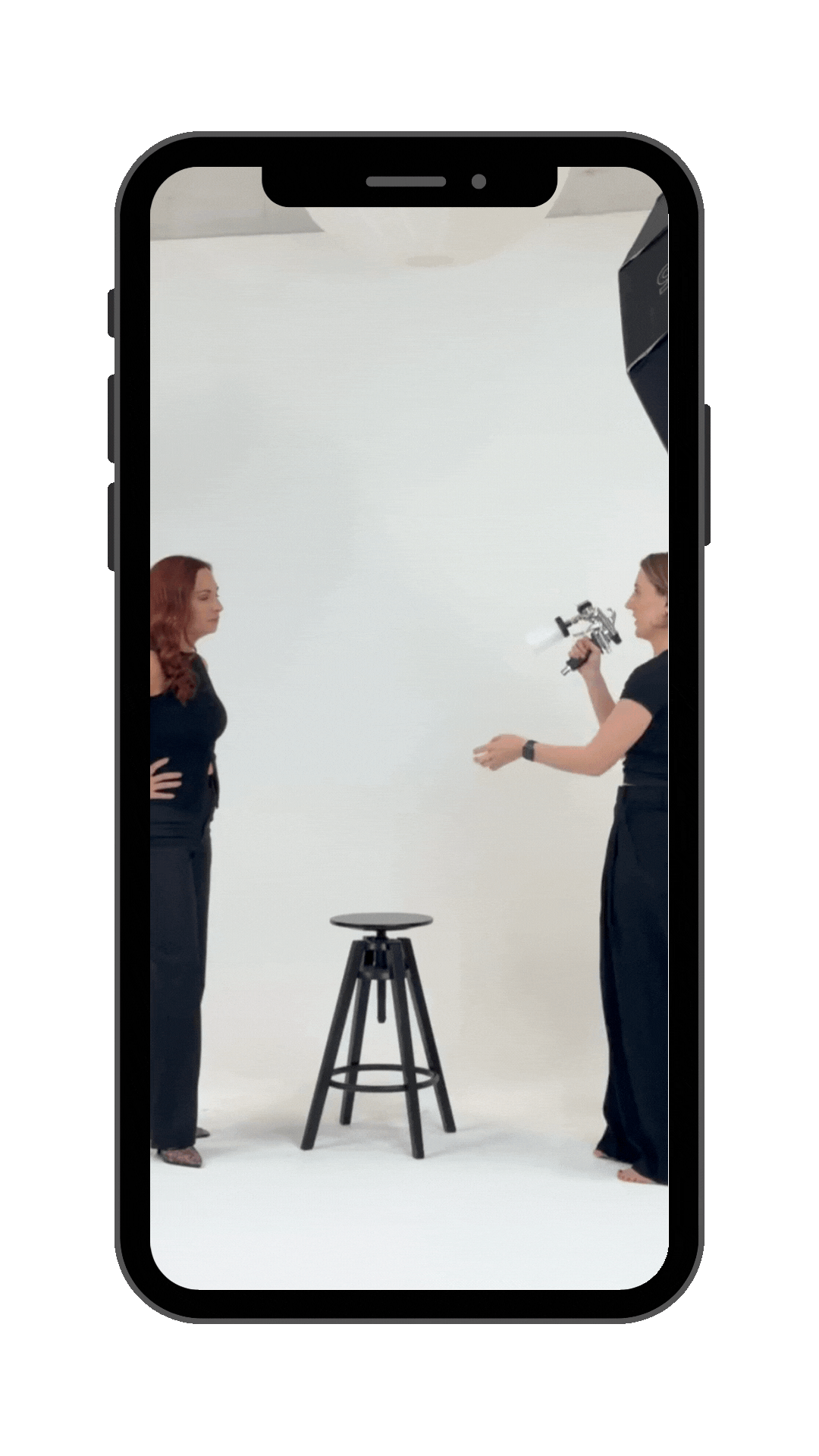 Two women in a photo shoot studio with a stool and a white background.