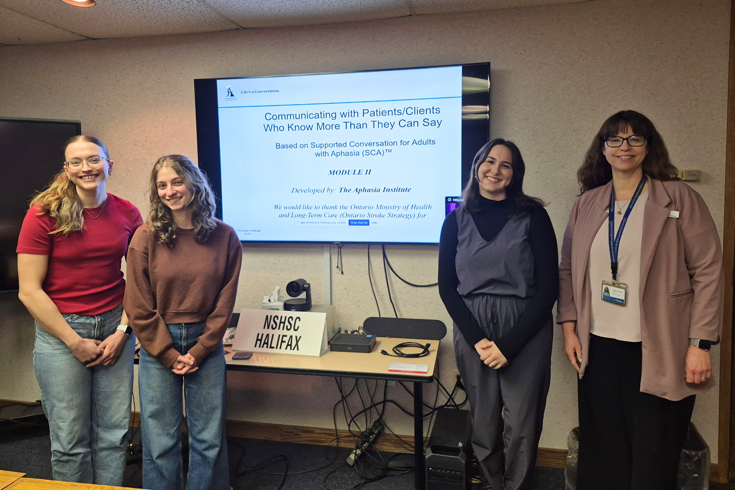 Four people, including one HSNS employee standing by a slideshow screen