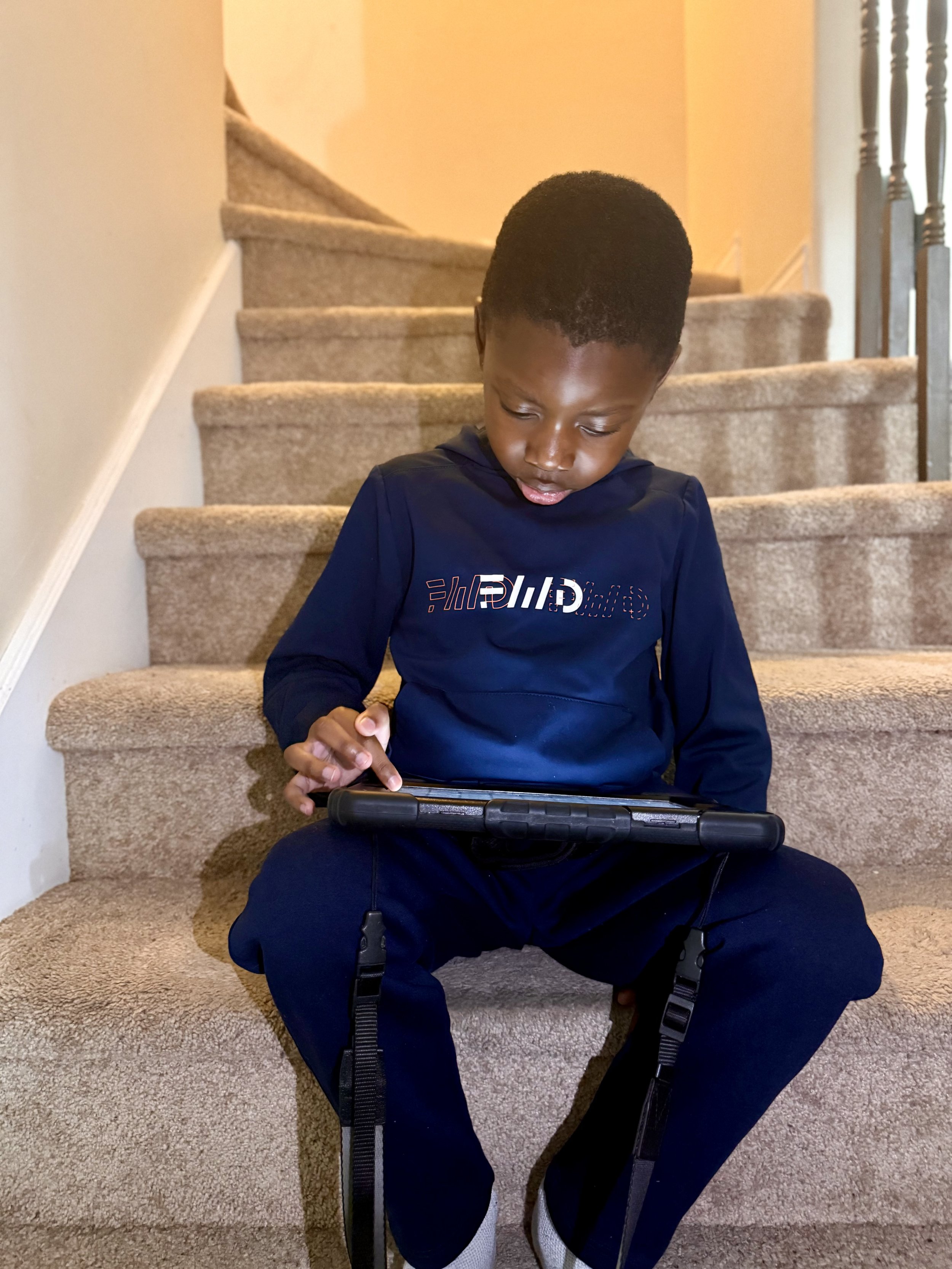 A young boy sitting on the stairs at home using his iPad
