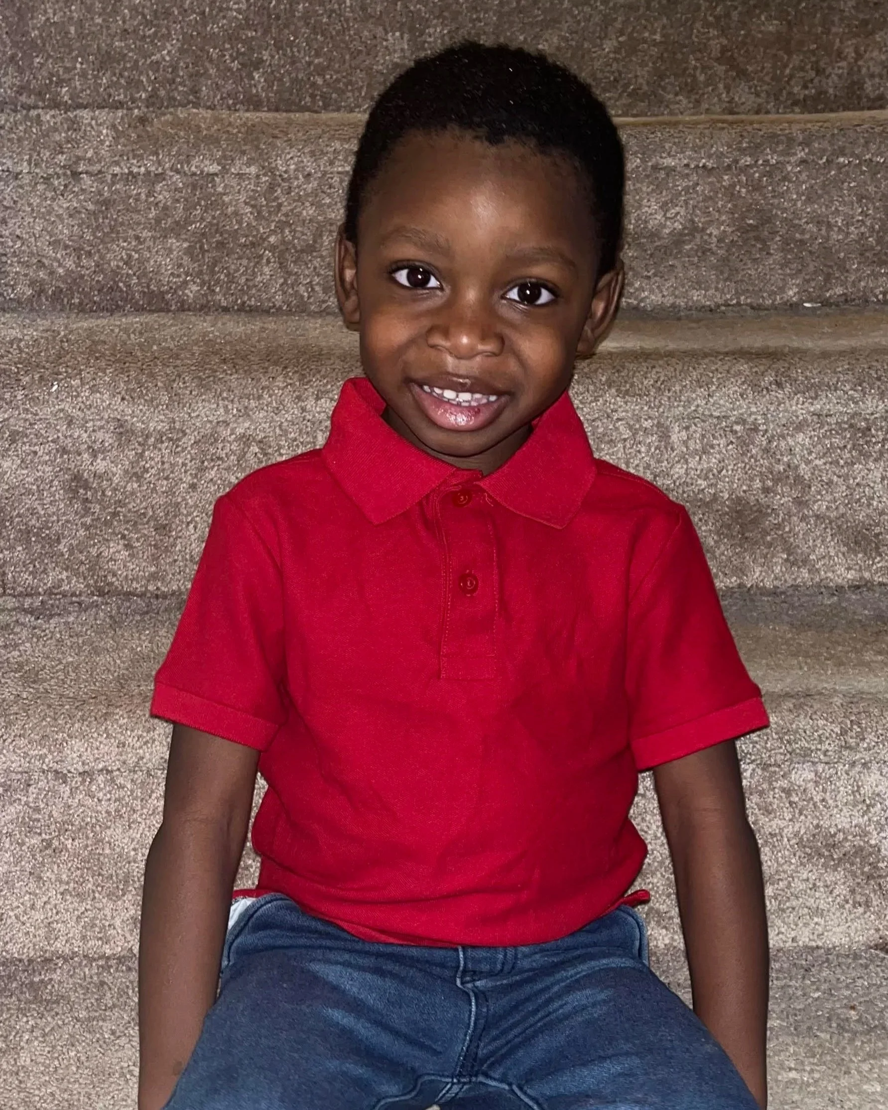 A child named CJ sitting on stairs in his home, smiling at camera