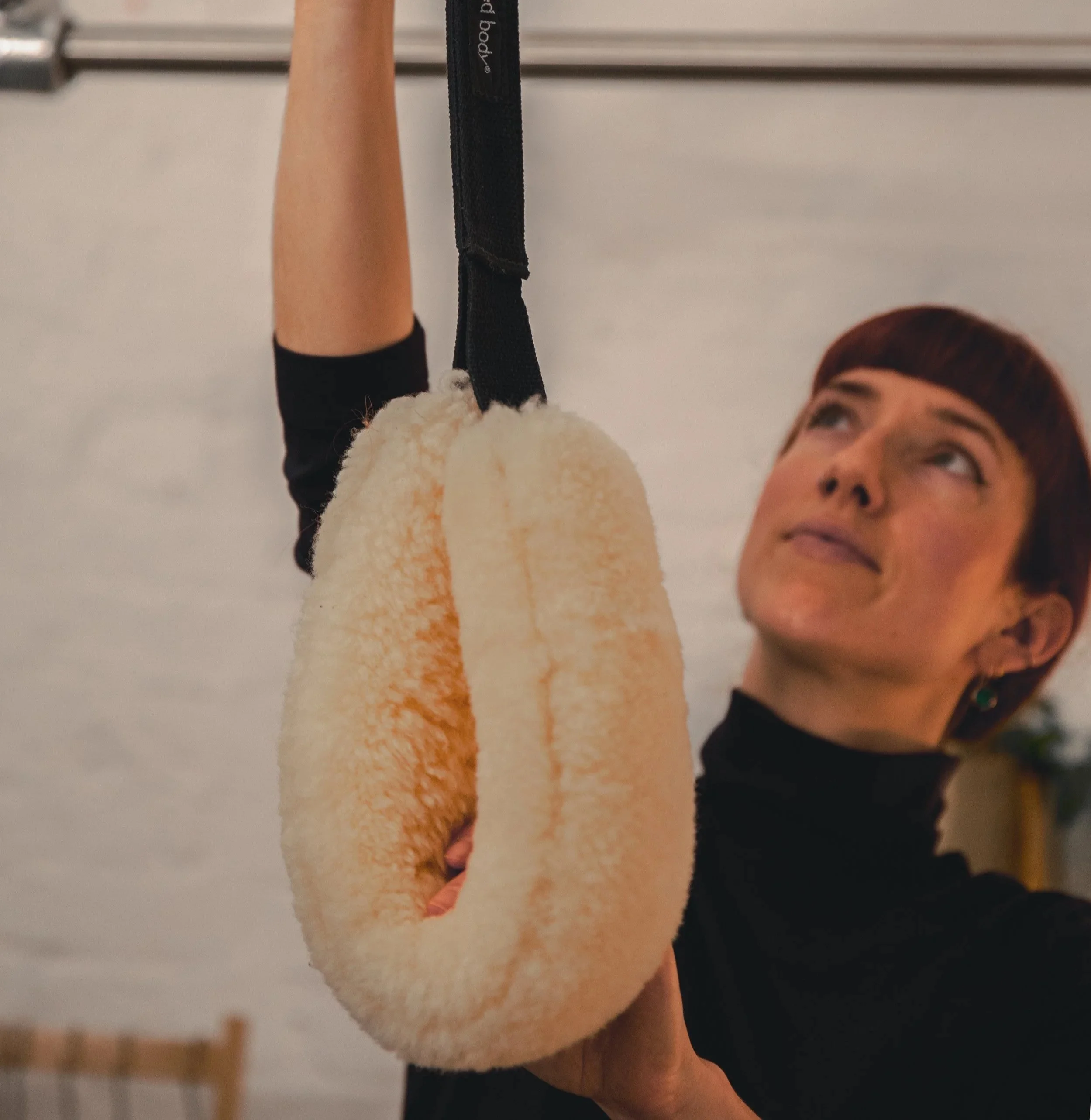 Close-up of black exercise straps and metal springs with yellow and red clips, likely part of a gym or Pilates machine against a blurred background.