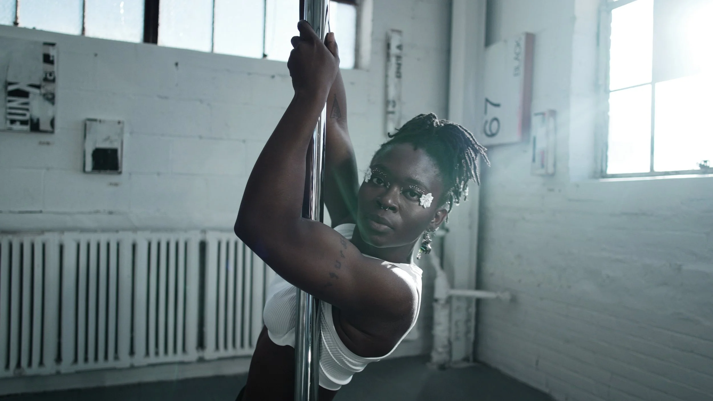 Person in a white top dancing on a pole in a room with bright natural light and a white radiator.