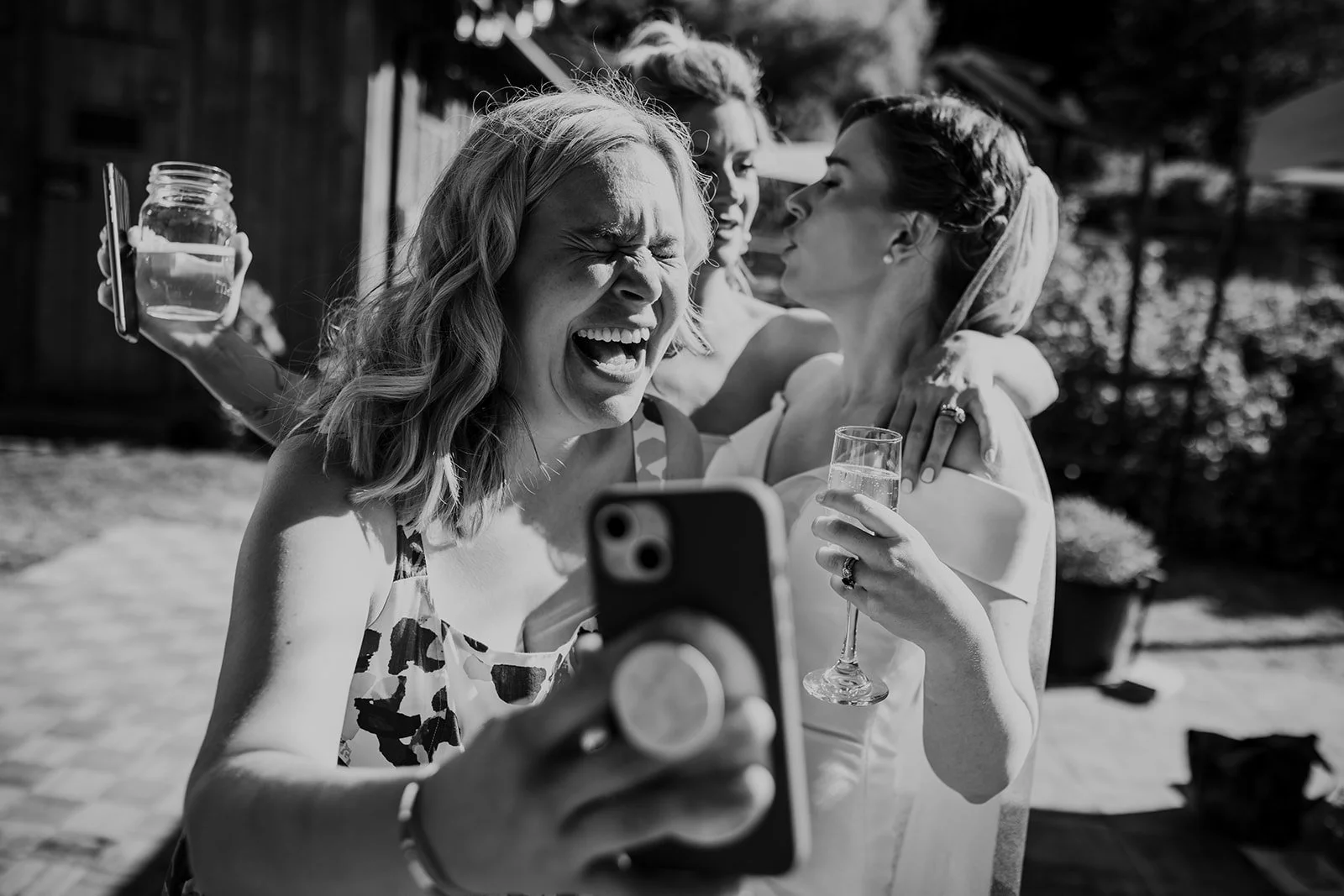 A candid wedding photograph of a bride and her bridesmaids laughing while taking a selfie. Wedding photography by Sea to Sky Studios at Endswell Farm on Bowen Island, BC.