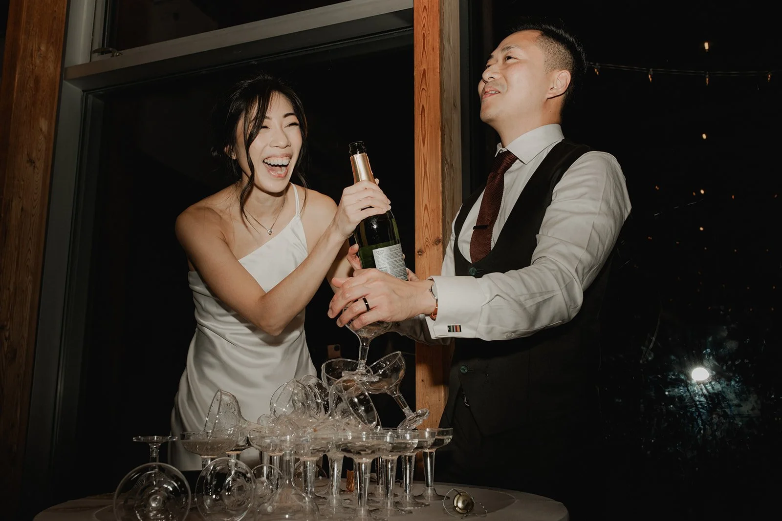A candid flash photography image of an Asian bride and groom and their champagne tower at their Vancouver wedding. Photography by Sea to Sky Studios.