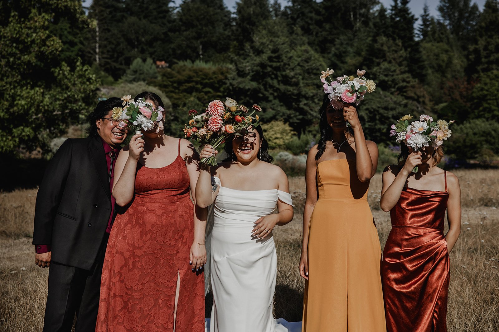  A bride and her bridesmaids holding flowers in front of their faces at an autumn wedding at UBC. Wedding photography by Sea to Sky Studios.