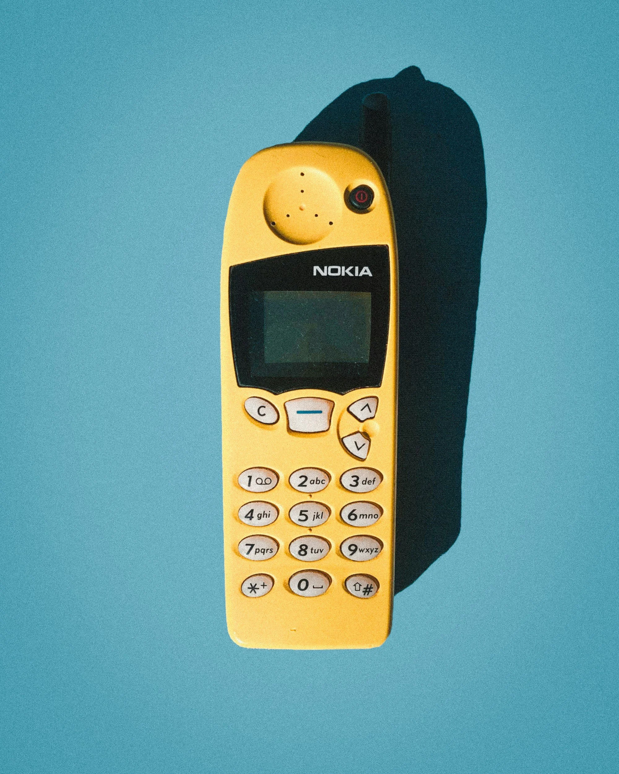 A yellow Nokia mobile phone with a small screen and physical keypad, casting a shadow on a blue background.