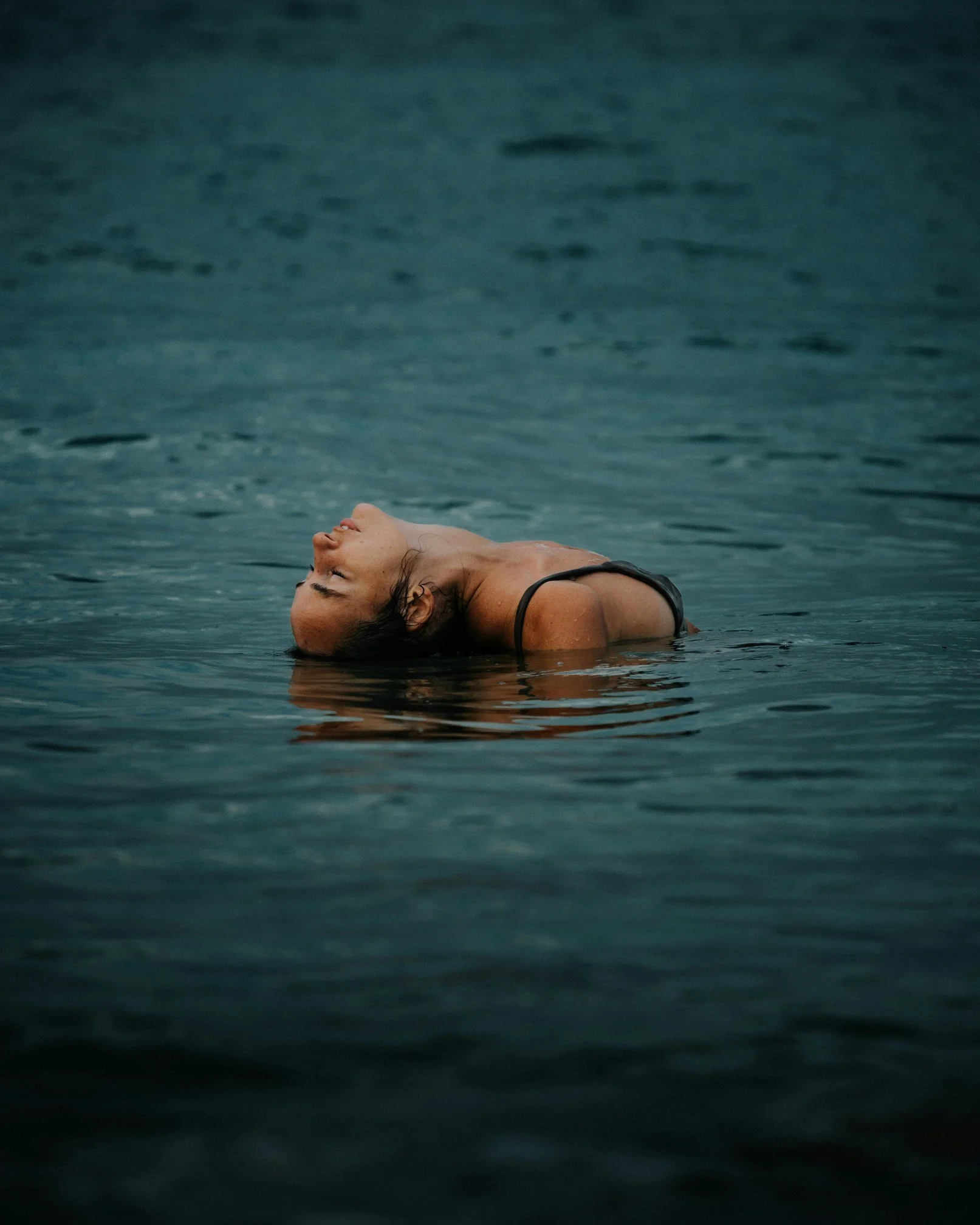 A woman floating in water with her head tilted back and eyes closed.