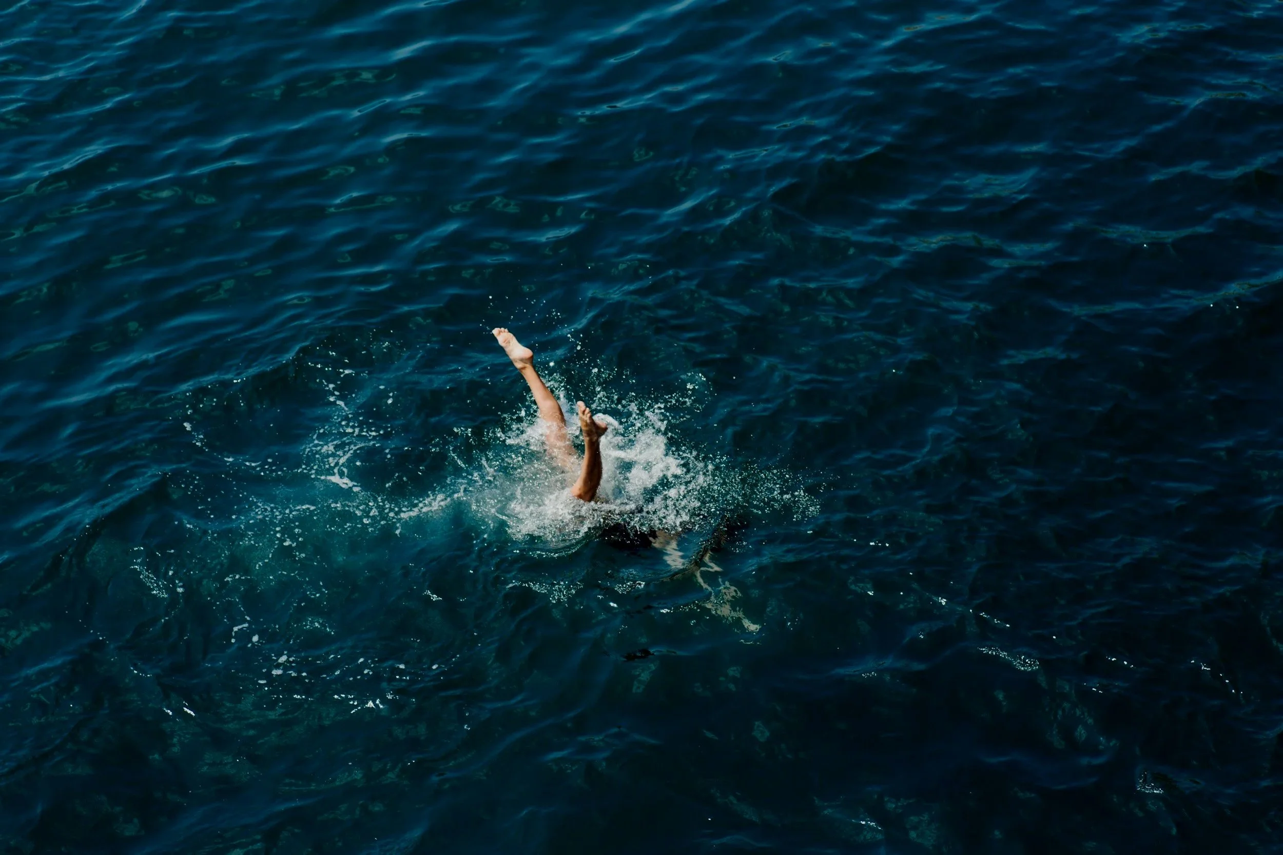 Person swimming in the ocean with arms raised above water, surrounded by deep blue waves.
