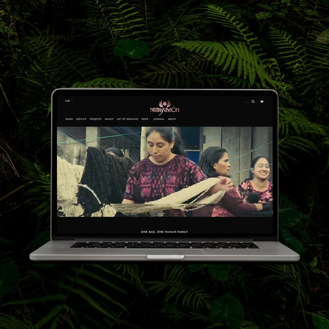 Laptop displaying a website about traditional weaving, with women using handloom in the image, surrounded by green fern plants.