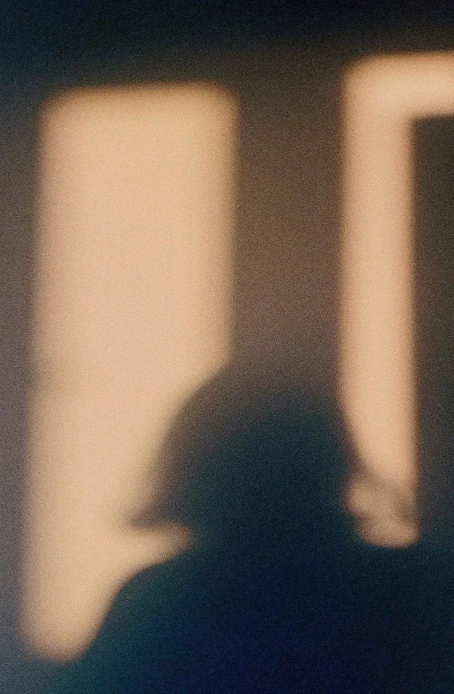 A blurry photograph of a person silhouette in front of a lighted window or wall, with warm light coming through a window or opening.