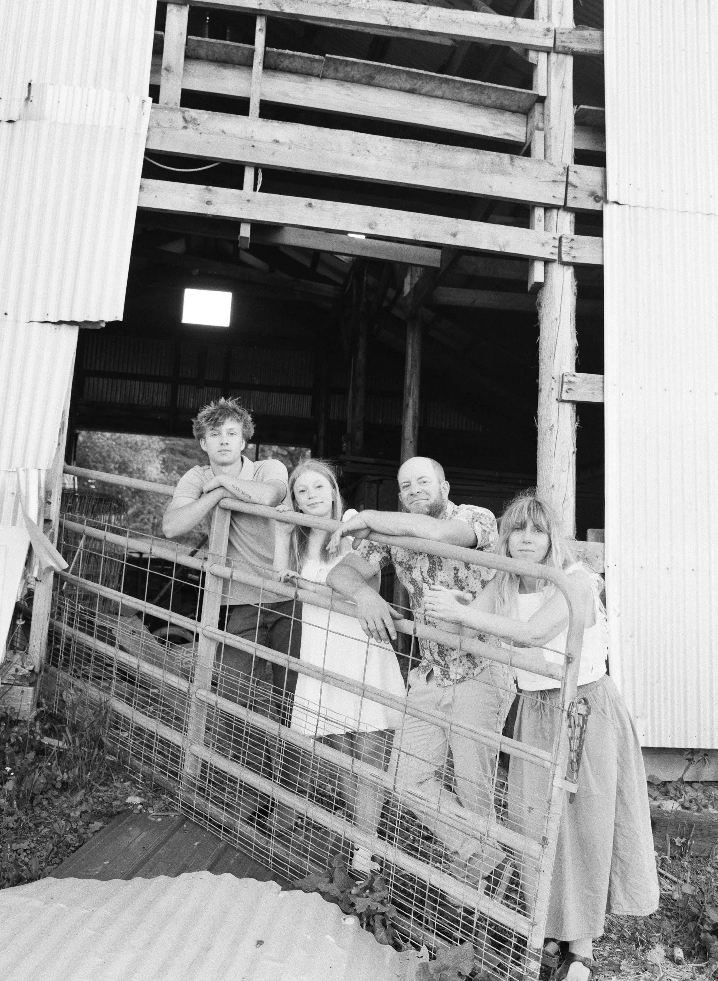 a family of 4 with older kids outside their barn on black and white film