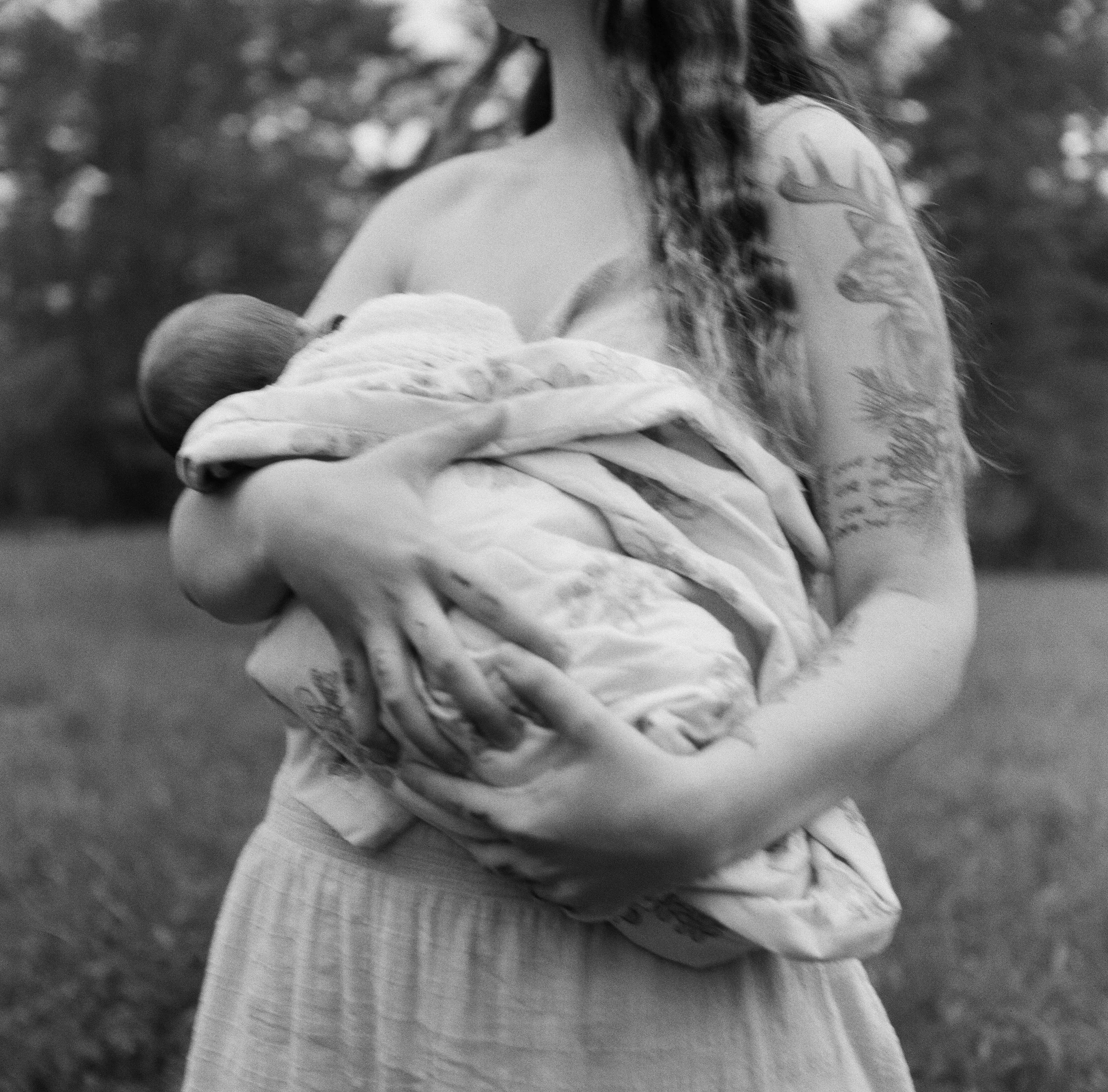 A mother holds her newborn daughter outdoors on film in maine