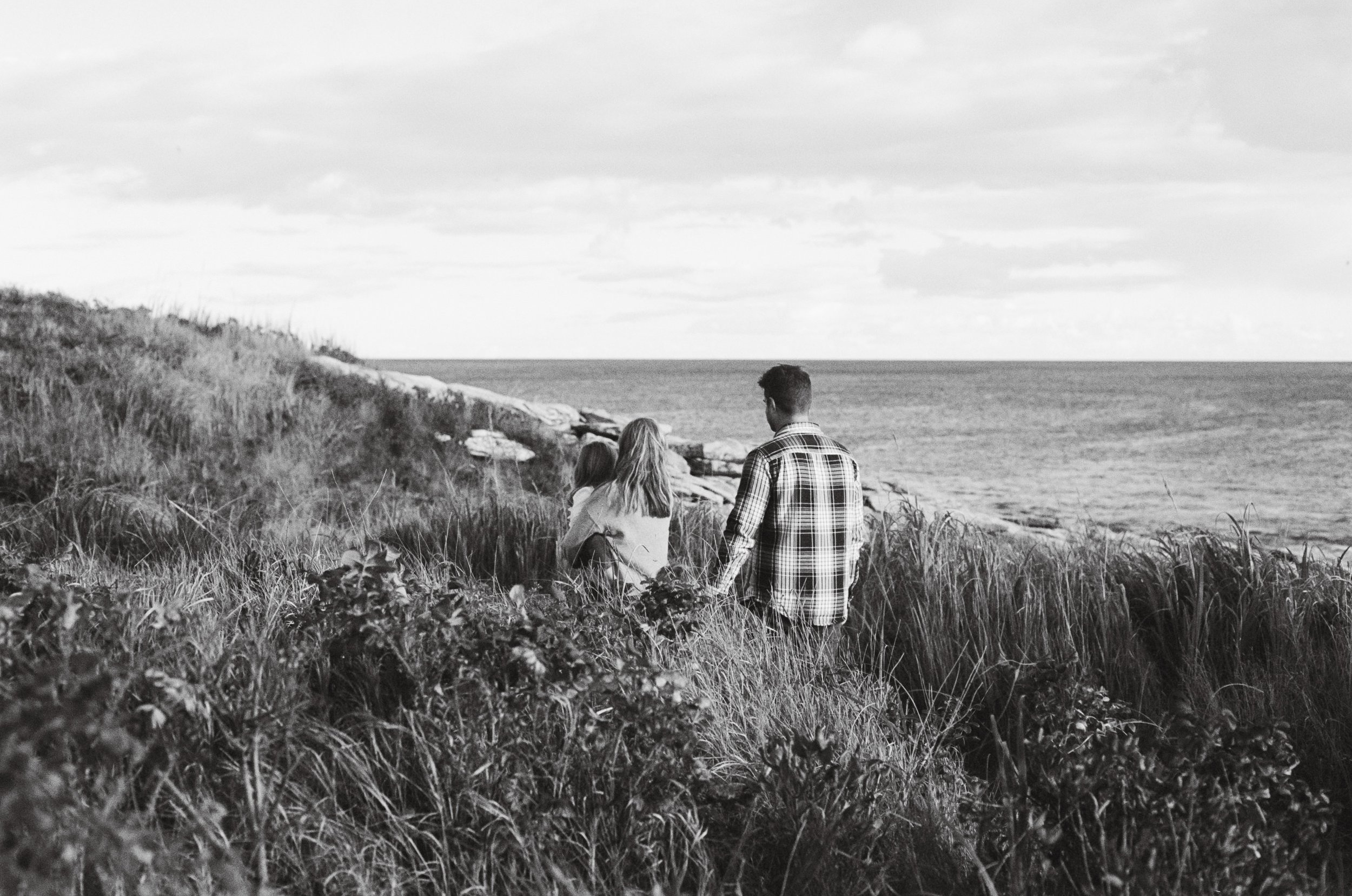 a family walks along a grassy beach in midcoast maine