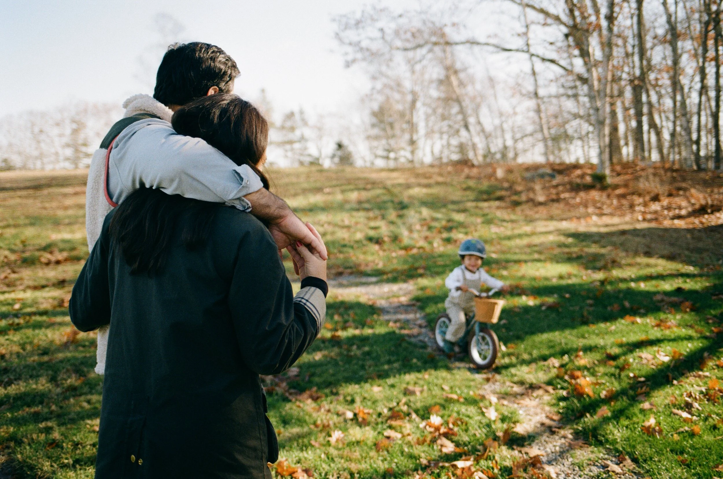 A boy rides his bike while the parents watch during a documentary film family session in midcoast Maine
