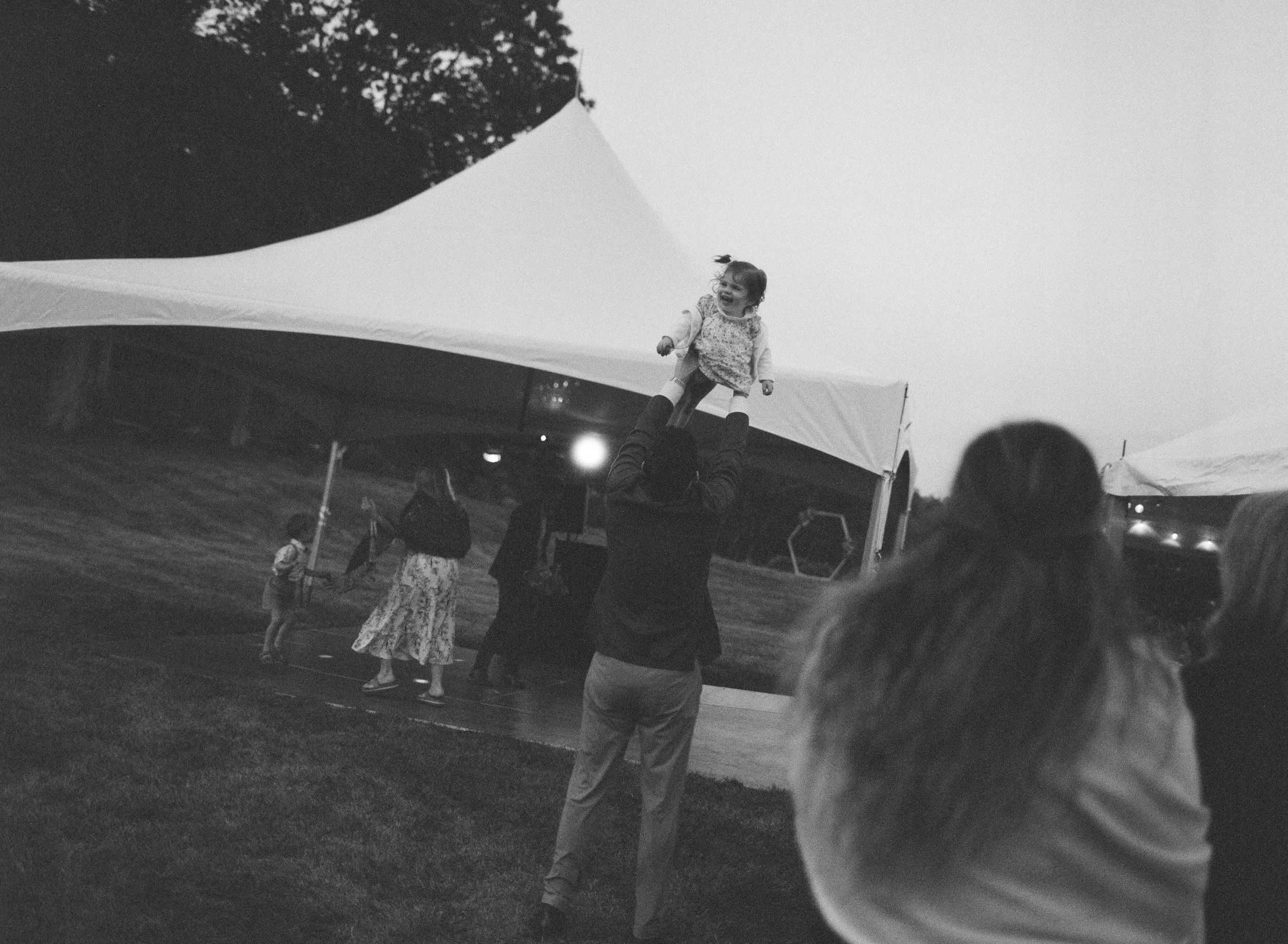 a man throws a child up into the air at abackyard tent wedding in Maine