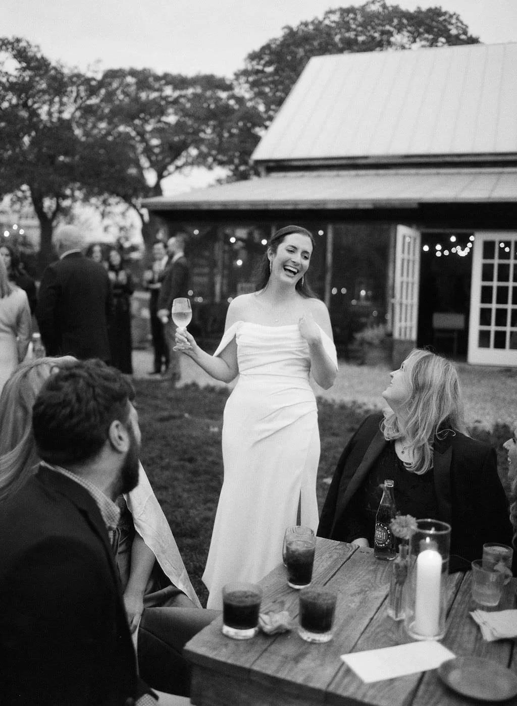 a bride laughs while holding wine glass talking to wedding guests on film in Maine
