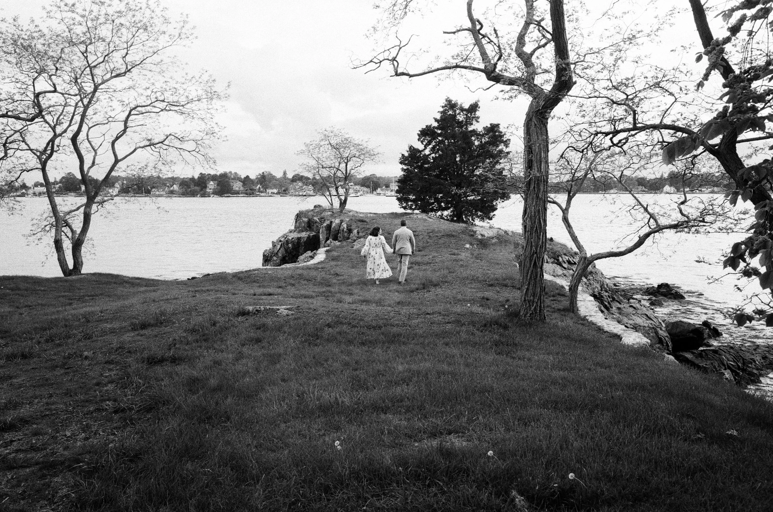 A couple walks down a stretch of grass on the coast of Maine for their wedding day on black and white film