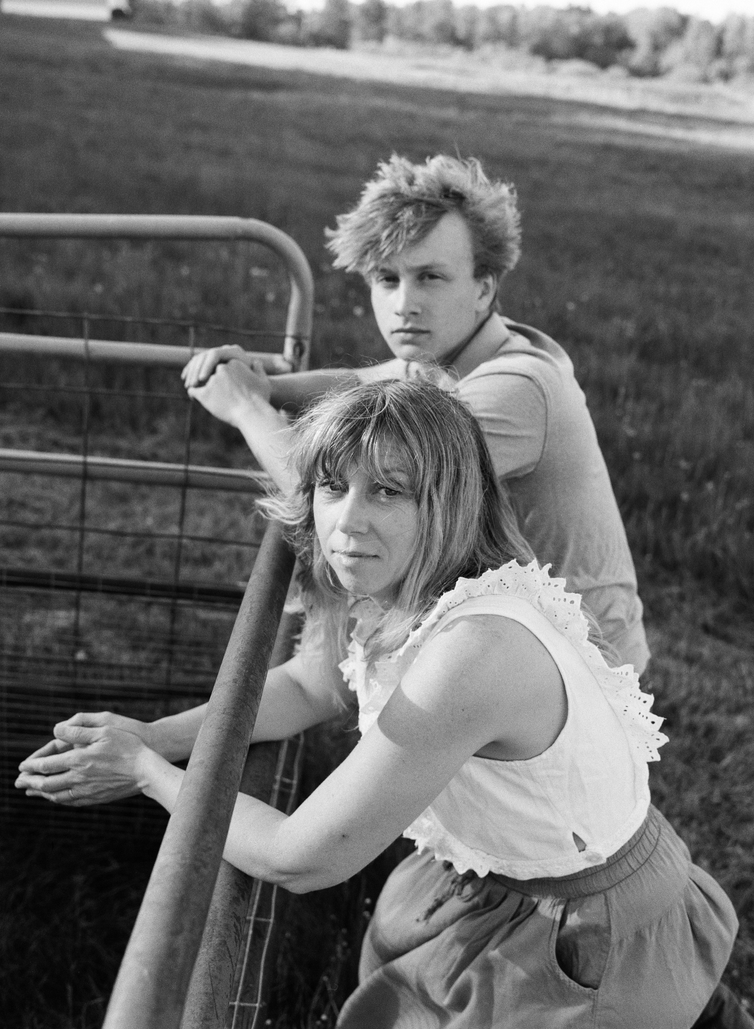 mother and son leaning against fence looking at camera on black and white film in maine