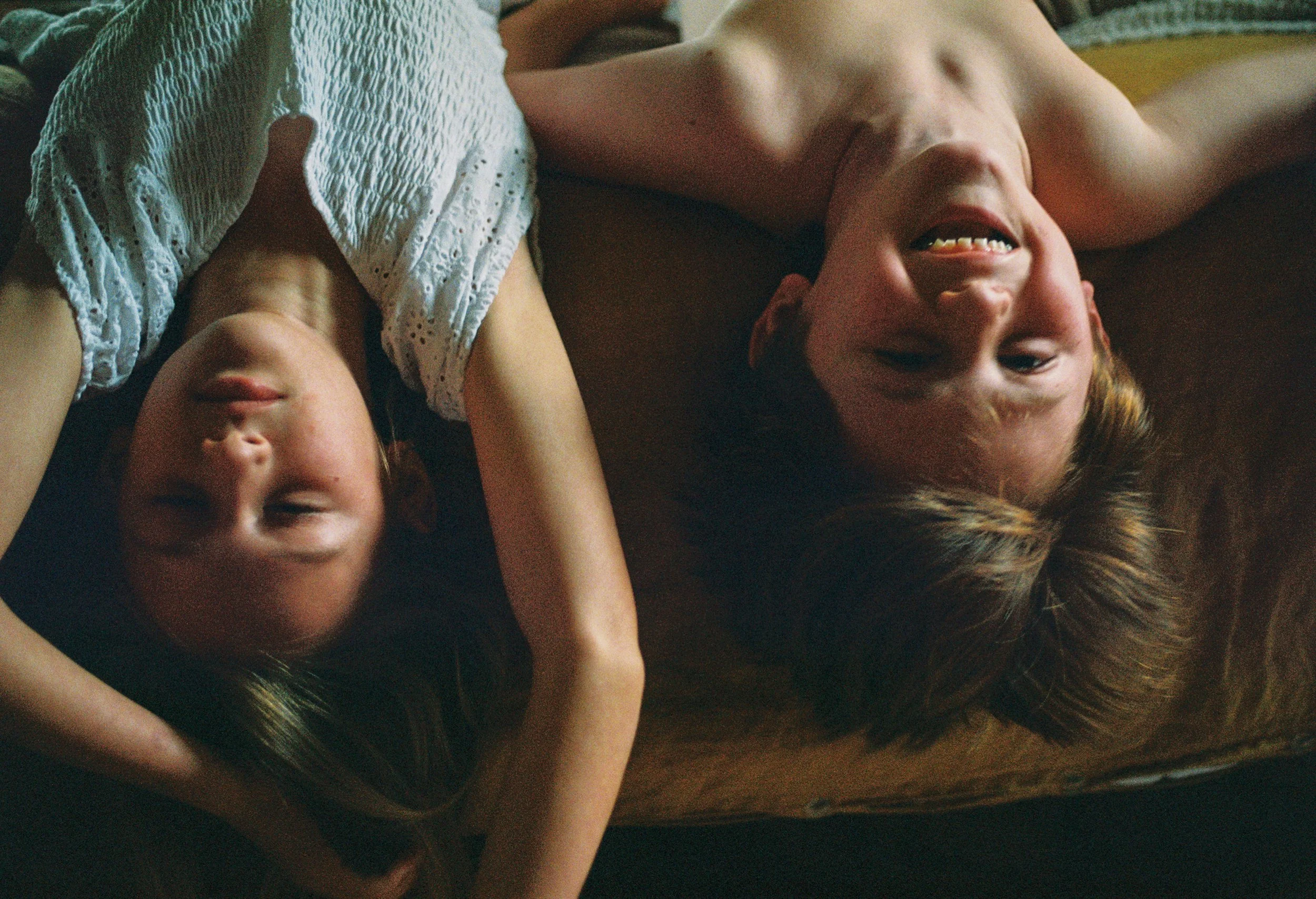 Two siblings smile as they fall over the bed during a family film session in new england