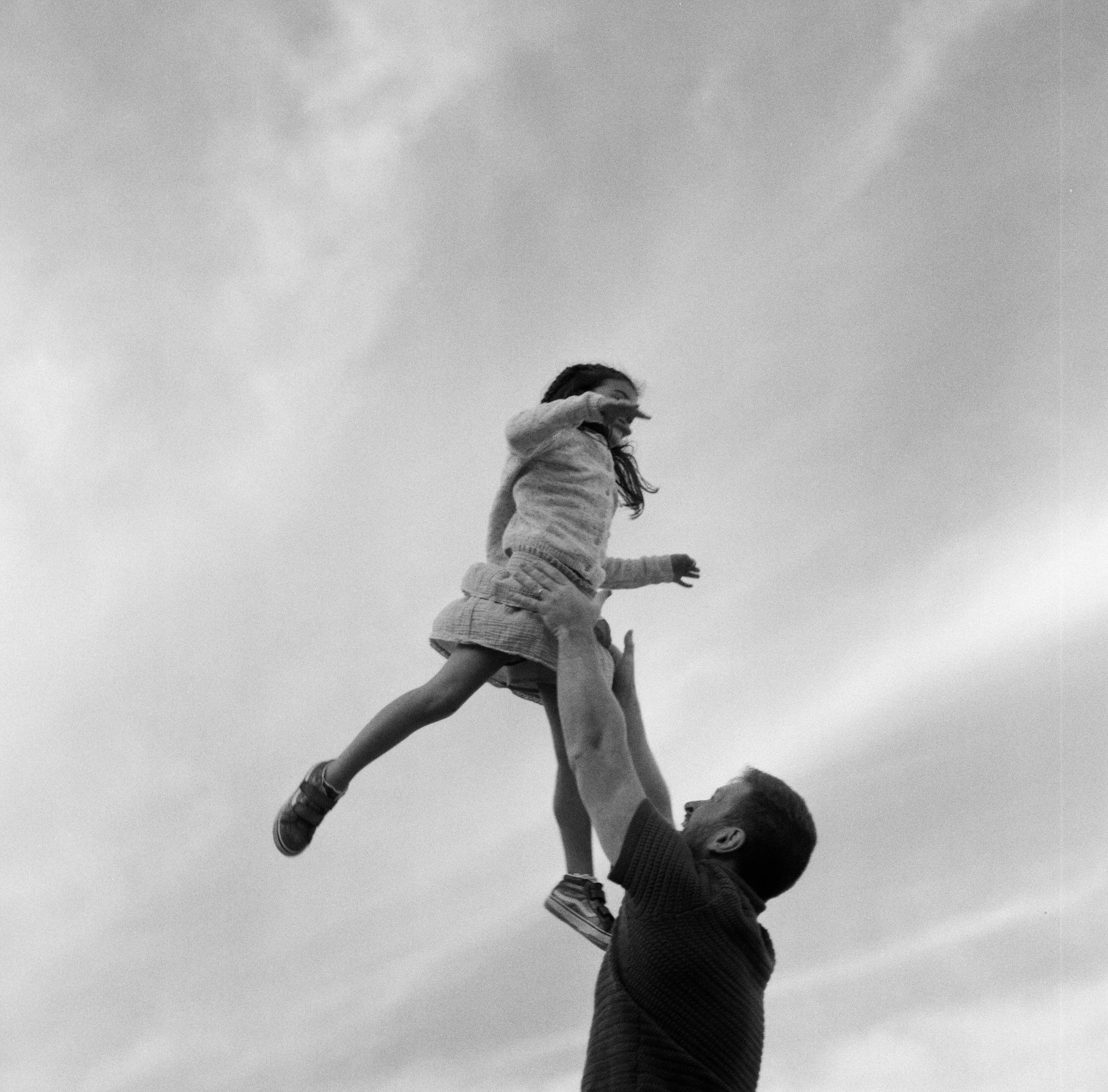 A dad tosses his daughter up into the air during this playful family session on film in midcoast Maine