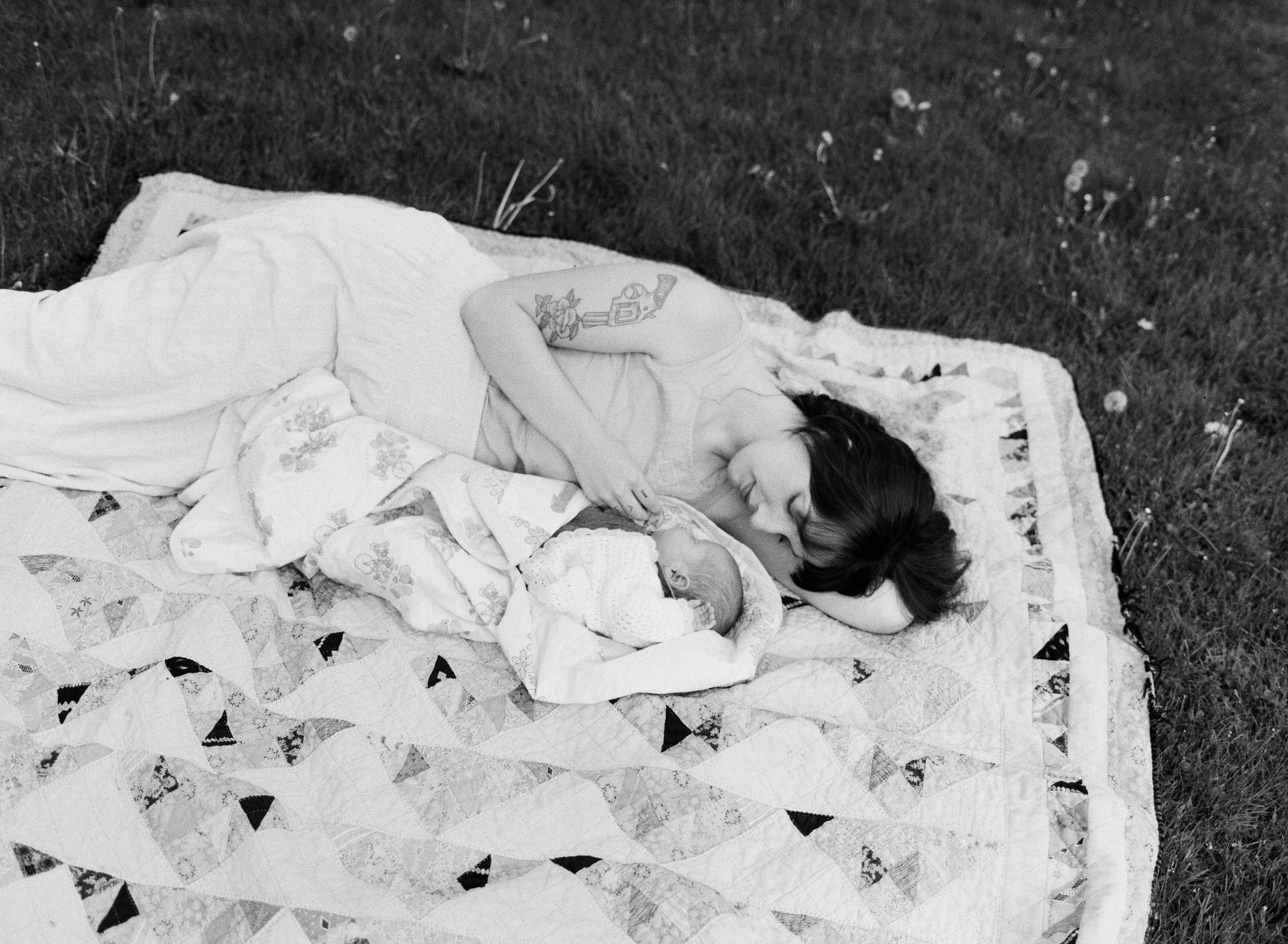 Newborn photography new england on film; a mother lies on a picnic blanket with her newborn baby at a park in midcoast maine