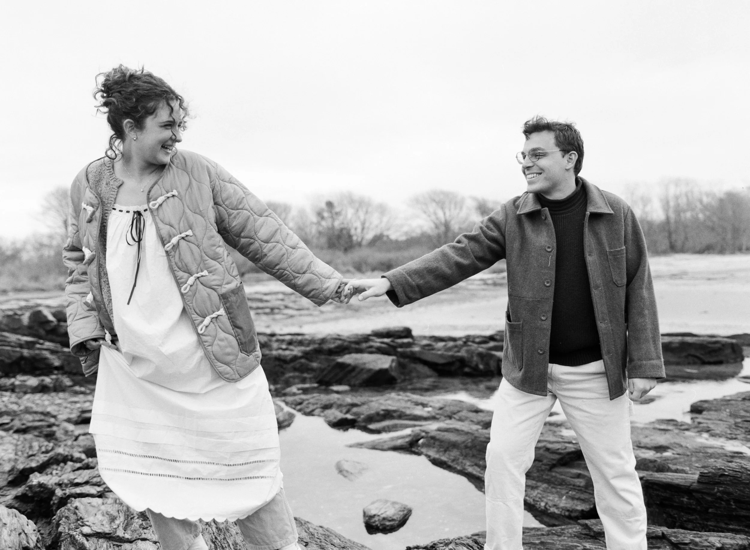 A couple holding hands while walking over rocks at kettle cove beach in maine