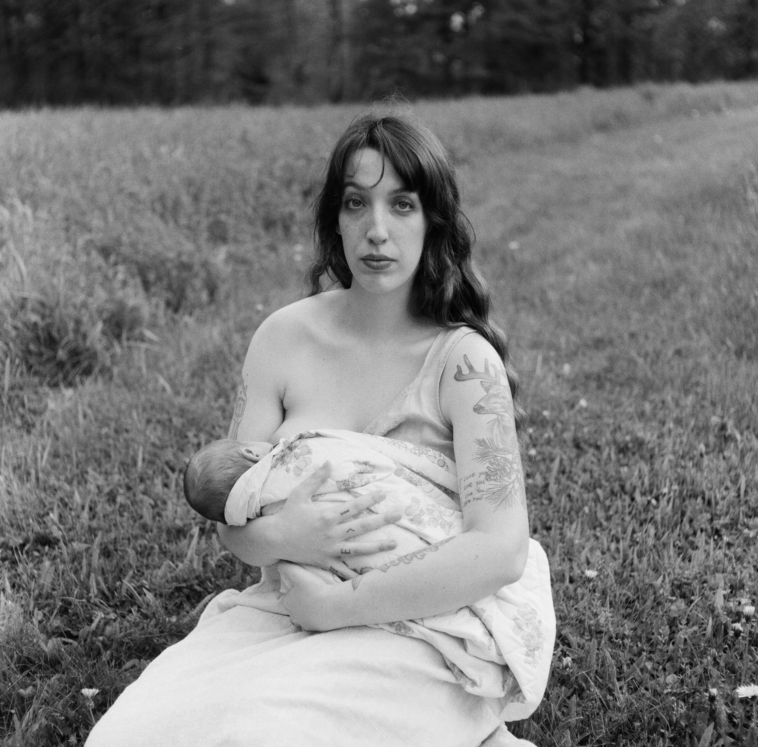 A mother stares directly at the camera while breastfeeding her newborn during a newborn film photography session in midcoast maine
