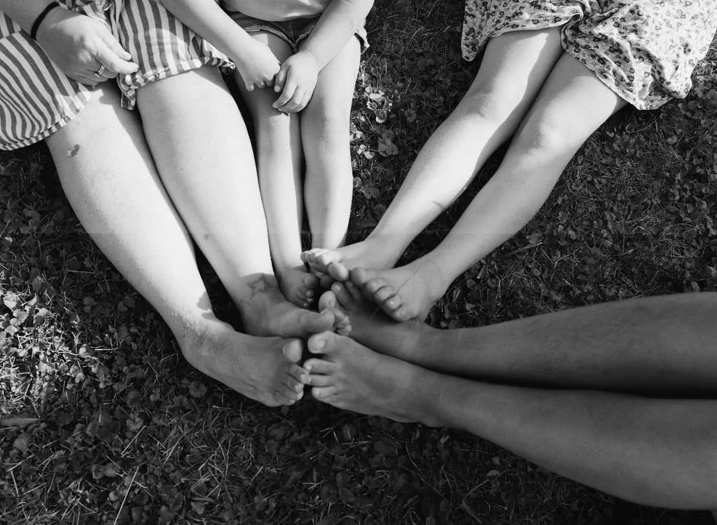 Families on film at home in Maine that feel candid and natural with everyones feet together in the grass of their backyard
