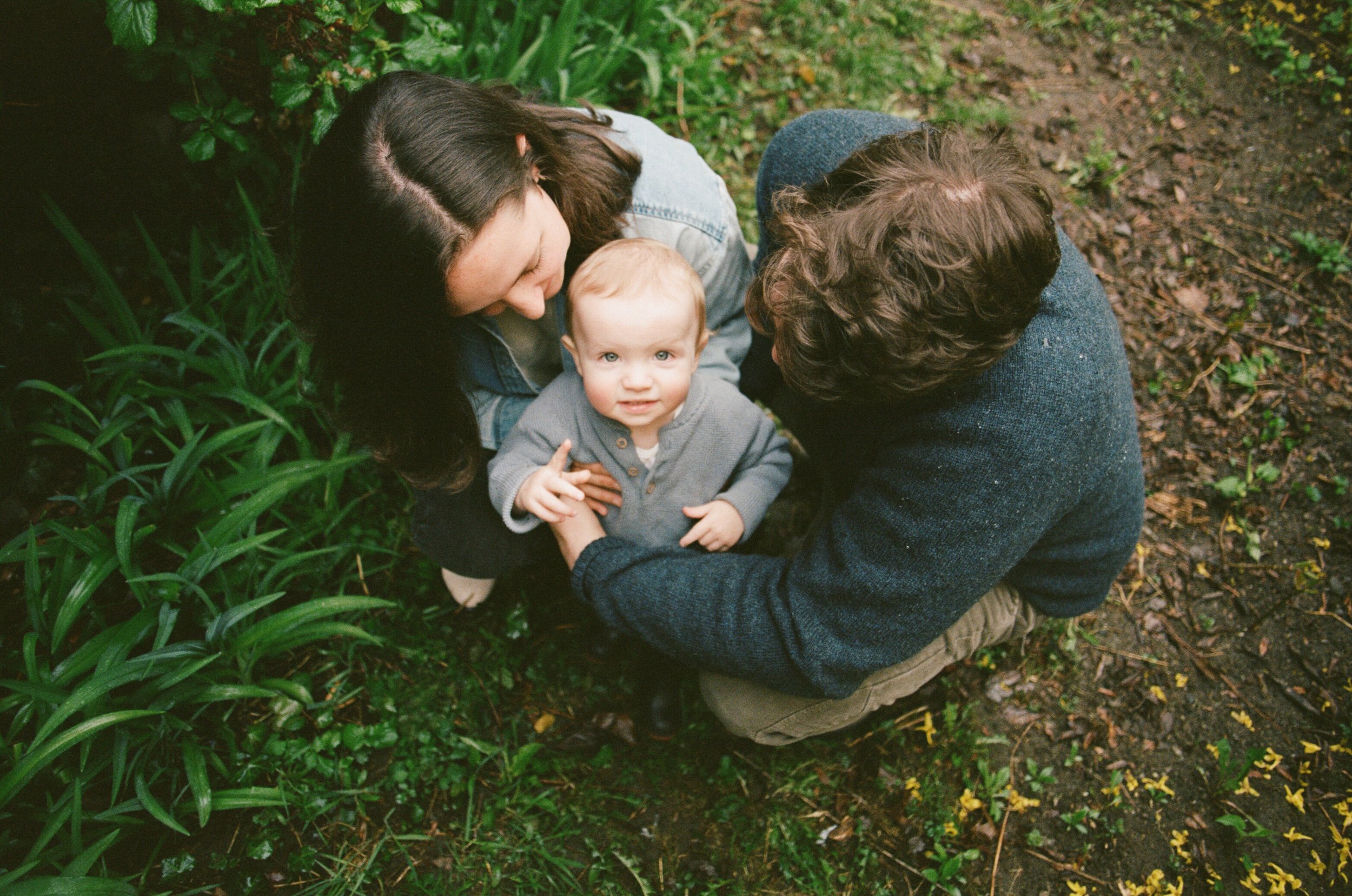 family of three crouching on ground at home in yard in portland maine